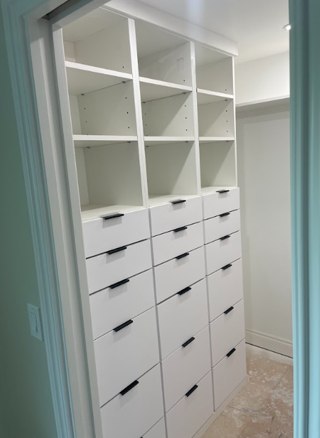 White built-in closet with open cubbies and many drawers in a narrow hallway