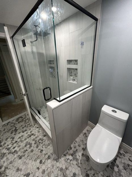 Modern bathroom with glass walk-in shower, white tile, and toilet beside a patterned floor