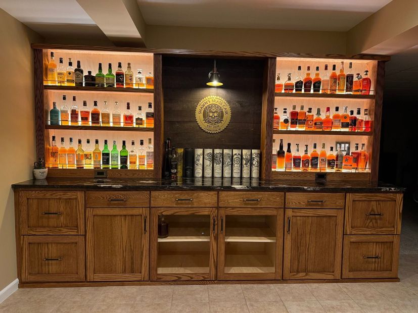 Wooden home bar with liquor bottles displayed on lit shelves and cabinets underneath