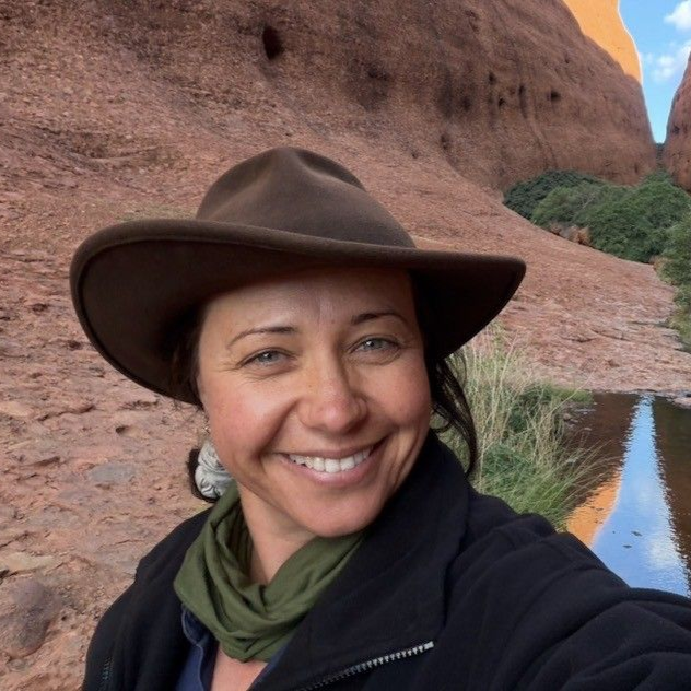 Janna smiling in a brown hat taking a selfie beside red canyon walls and a narrow water channel