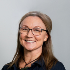 Portrait of a smiling woman with glasses against a plain gray background
