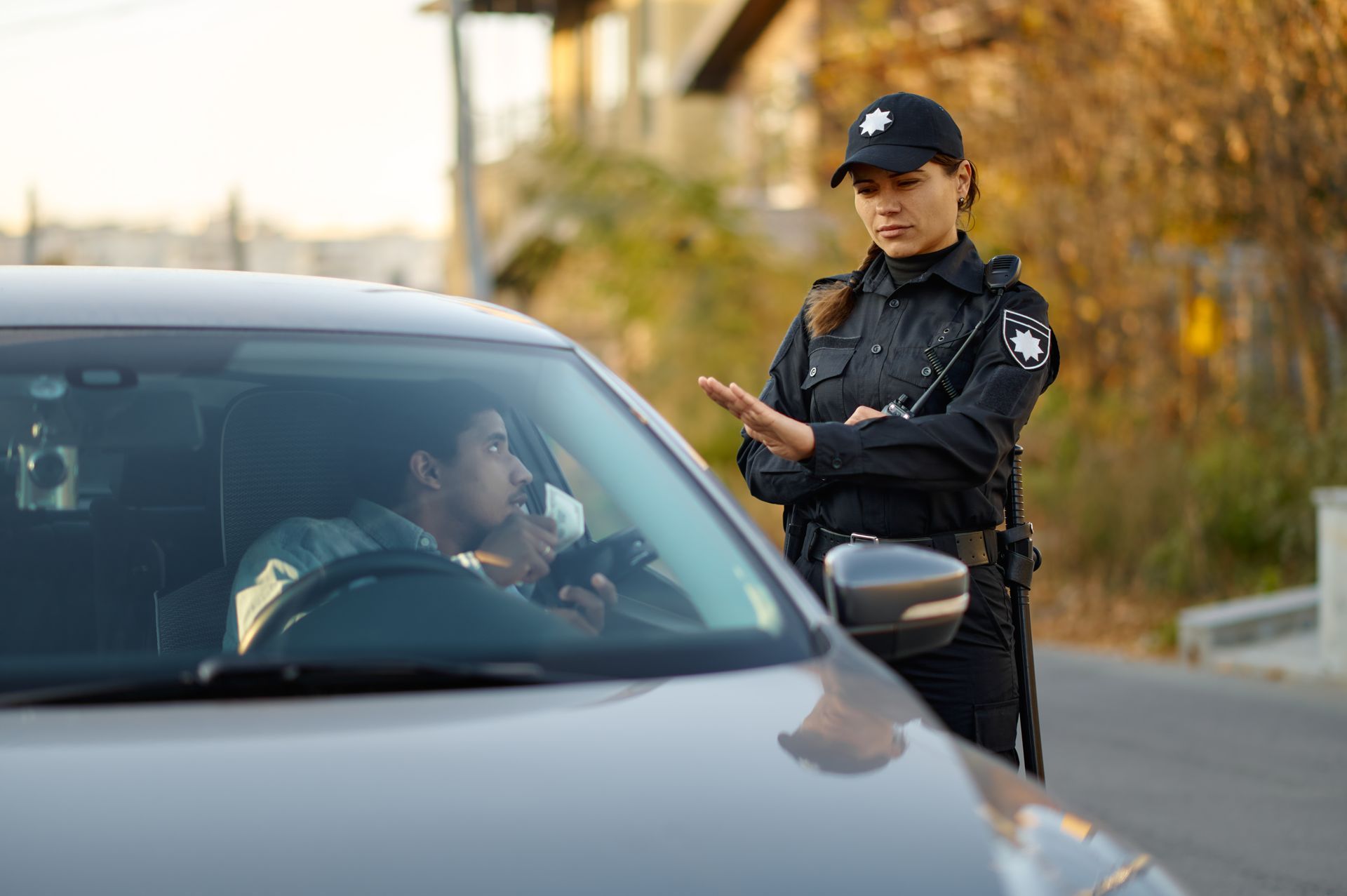 A police officer in uniform signals a driver to stop as they provide a breathalyzer sample inside a parked car.