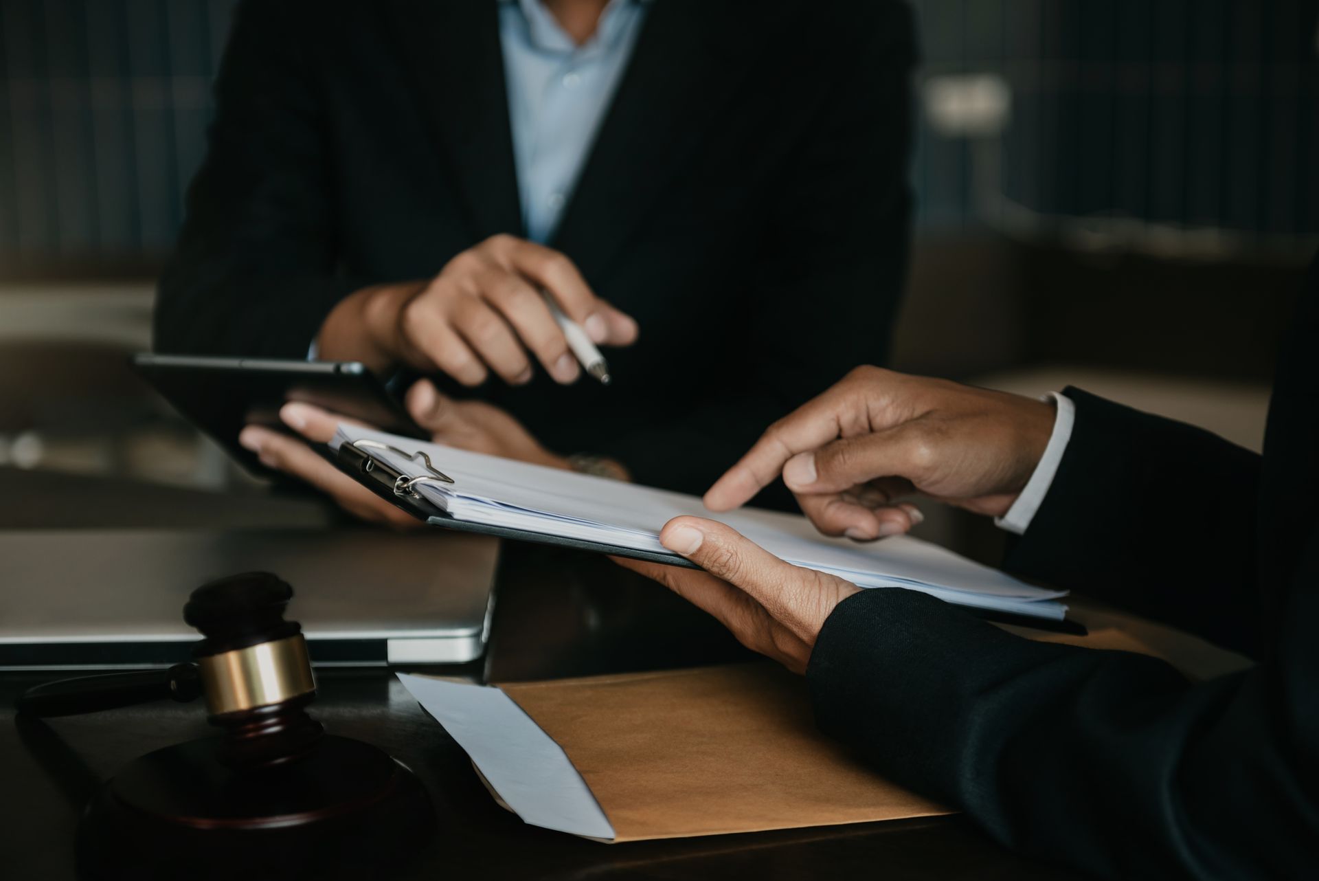 Two professionals in business attire review legal documents at a desk featuring a wooden gavel.