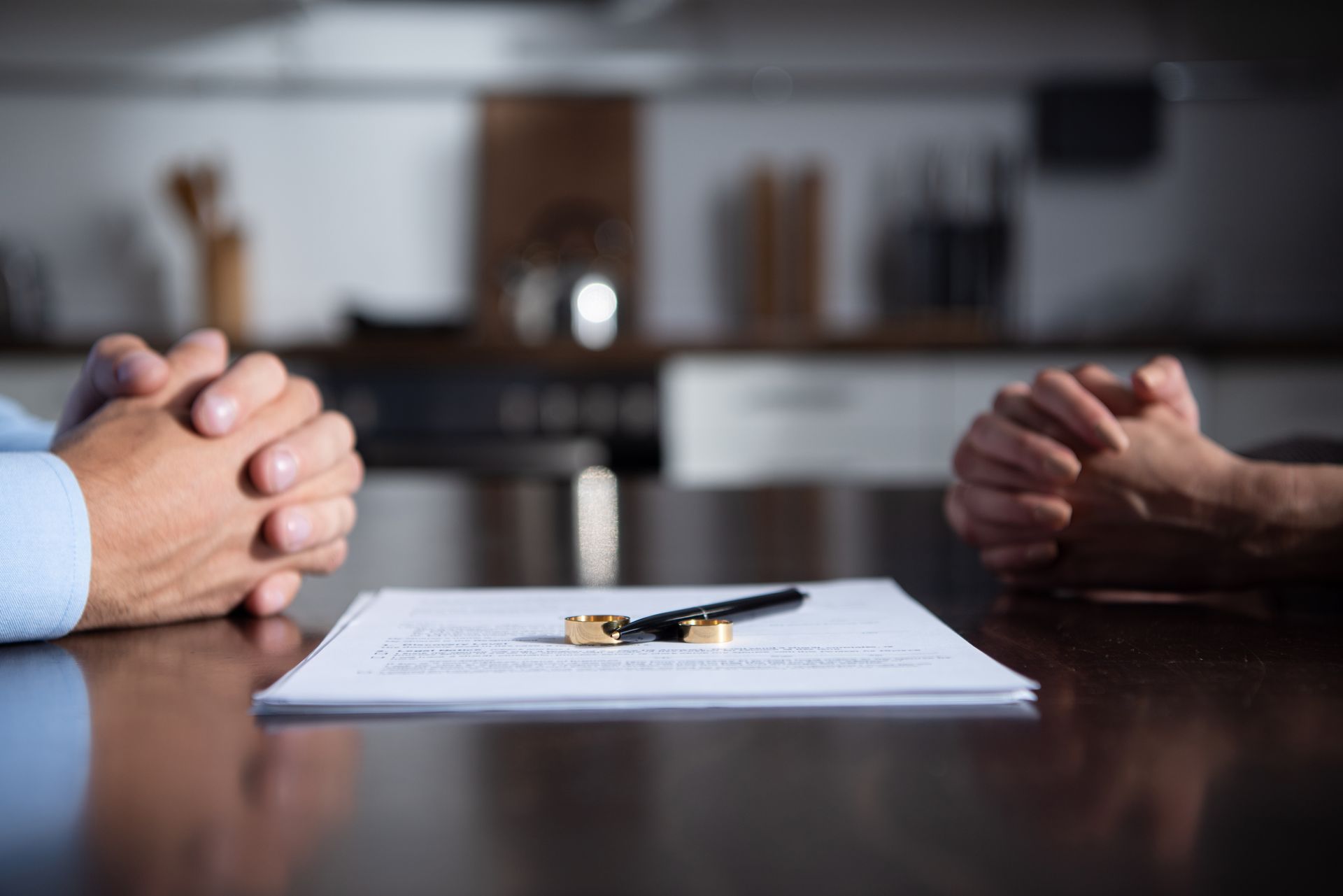 Two wedding rings sit on a white desk in front of a person signing legal documents.