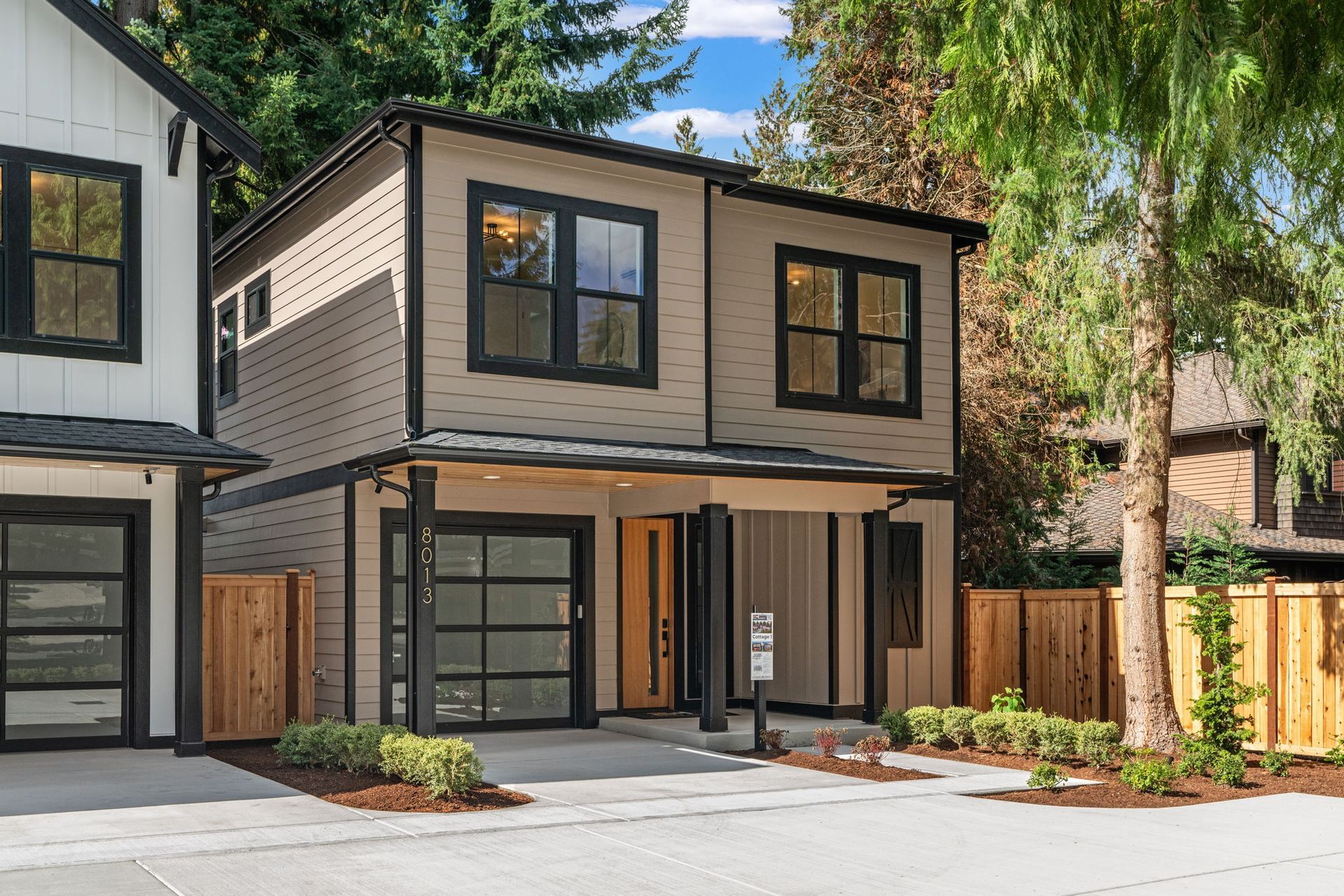 Cottage 1 house exterior render. Modern two-story homes with garage and front door. Dark gray and light tones.