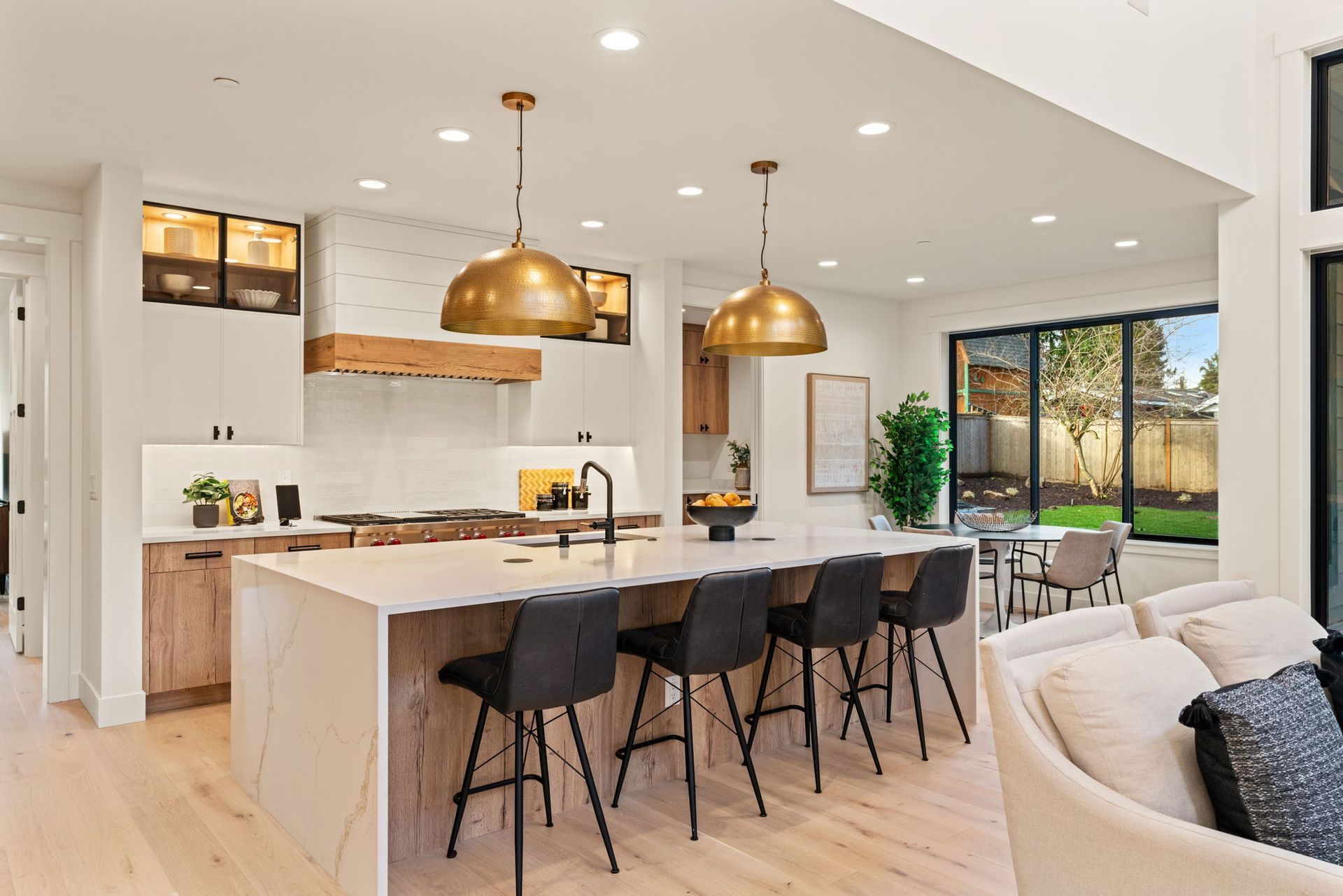 Modern kitchen with island seating, pendant lights, and backyard view through sliding doors.