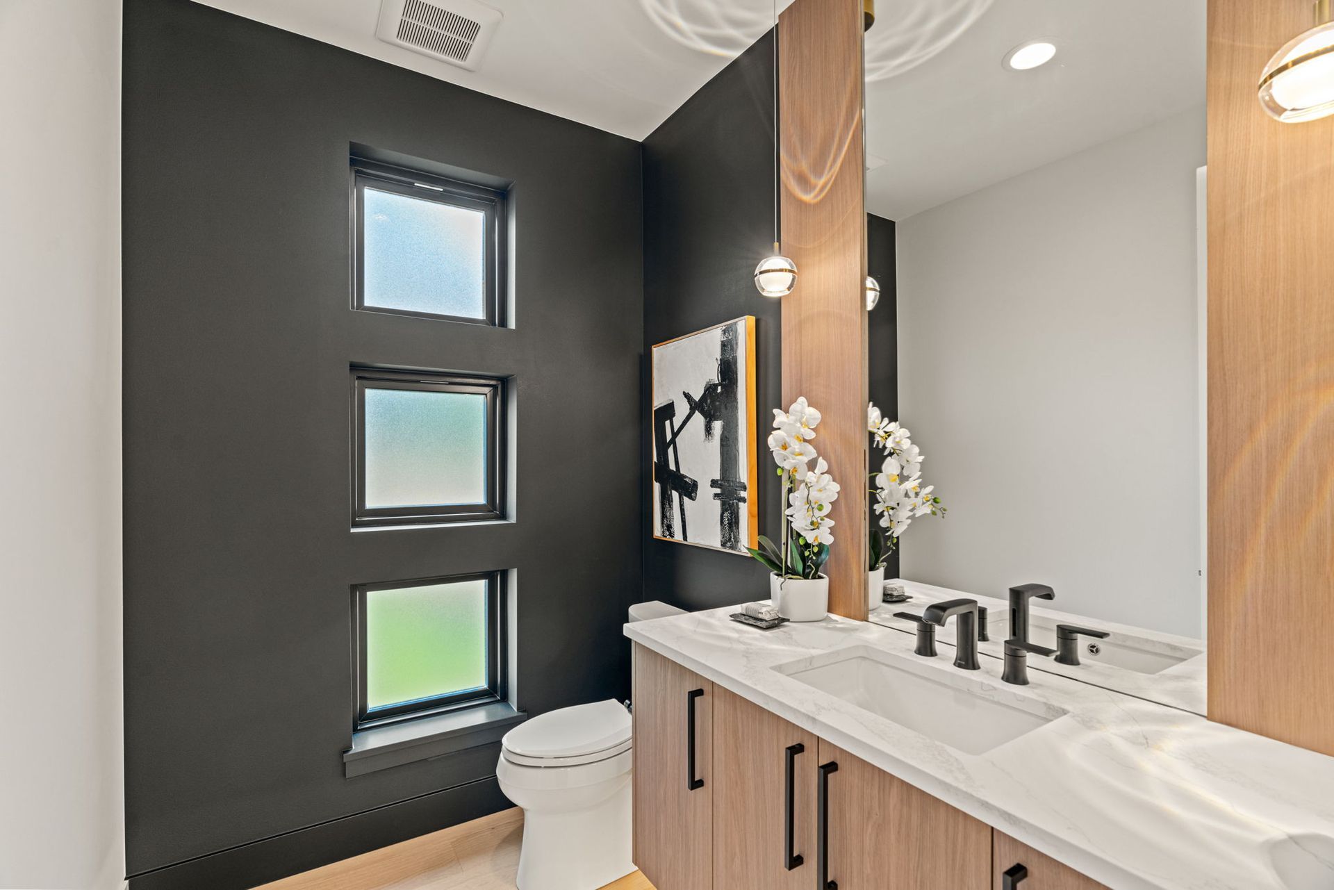 Modern bathroom with dark wood cabinets, marble countertops, and a freestanding tub by a window overlooking trees.