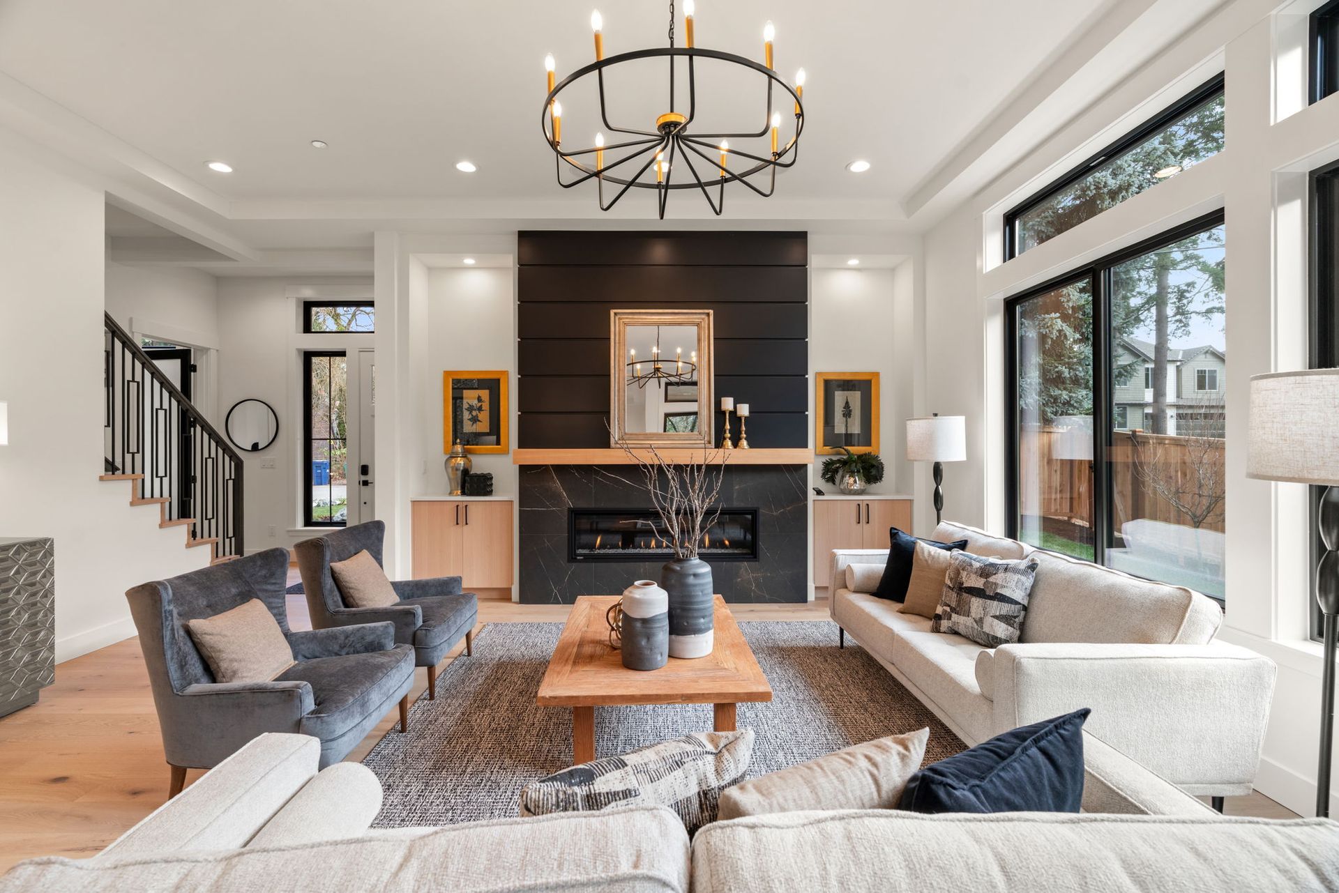 Living room with fireplace, sofas, armchairs, hardwood floor, and a black and gold chandelier.