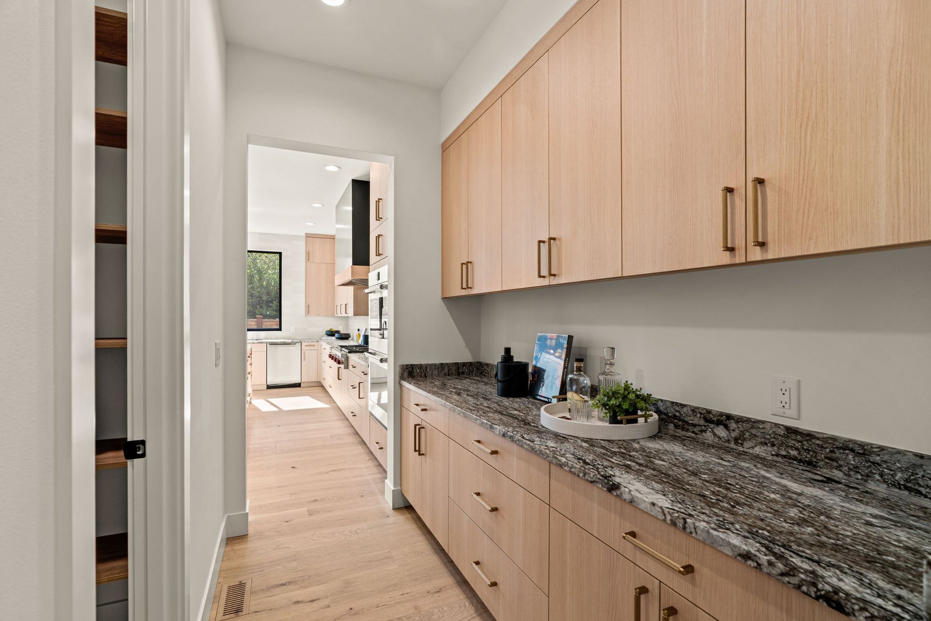 Narrow kitchen hallway with wood cabinets, granite countertop, and view into a bright kitchen beyond