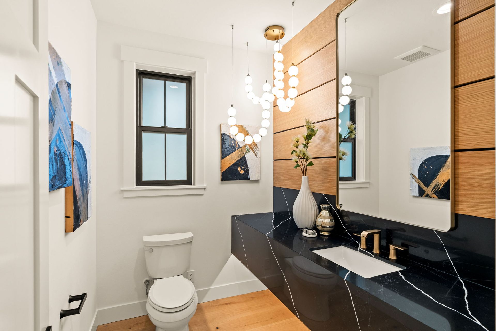 Stylish powder room with a black countertop, wooden accent wall, and decorative chandelier.