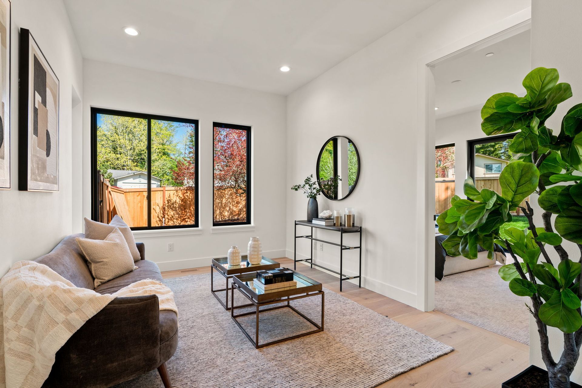 Bright modern living room with gray sofa, coffee table, large windows, and a leafy plant