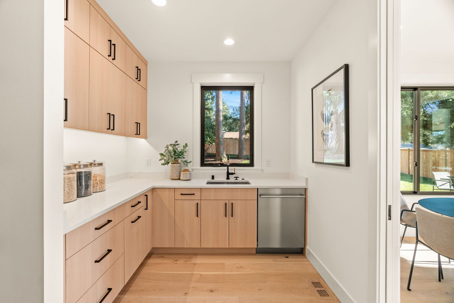 Modern butler's pantry with light wood cabinets, white countertops, and stainless steel dishwasher.
