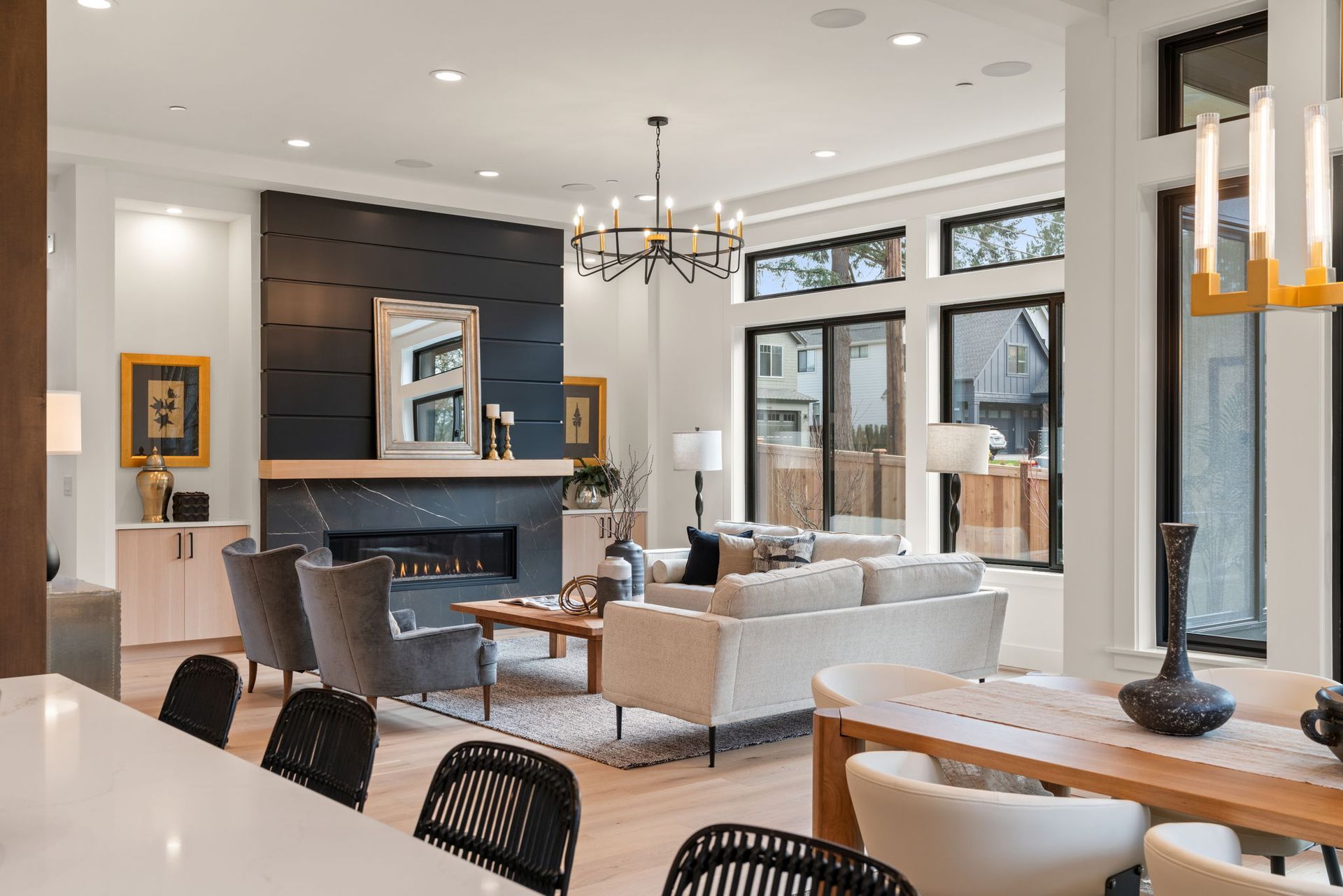 Modern living room with fireplace, neutral colors, large windows, chandelier, and a dining table.