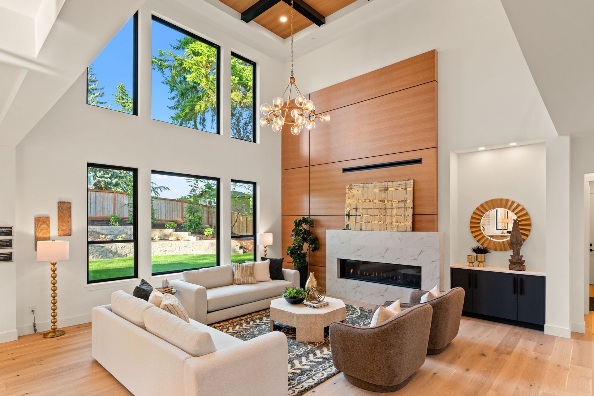 Bright modern living room with high ceilings, large windows, beige seating, and a fireplace centerpiece