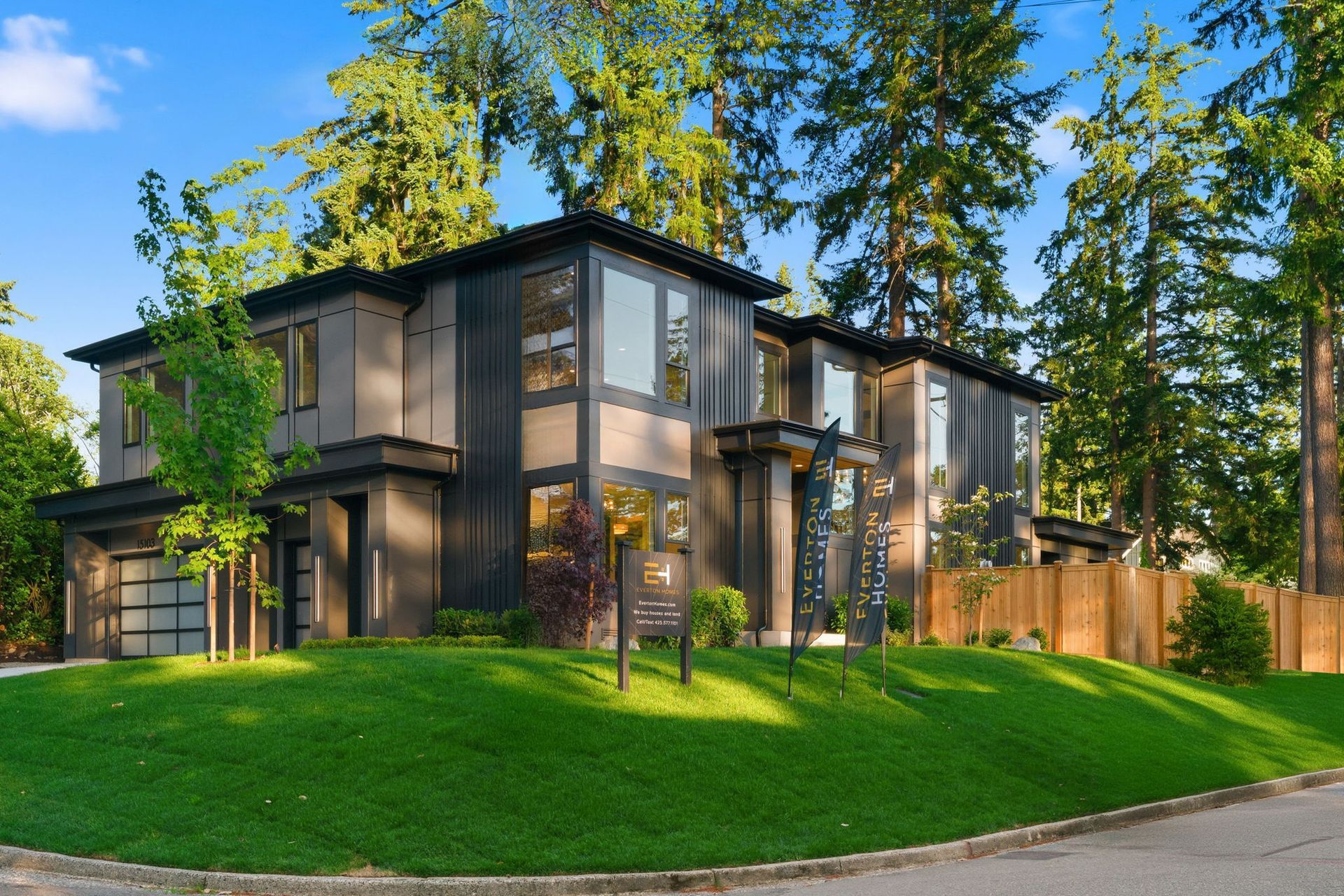 Modern two-story glass-and-wood house with a green lawn and tall trees in a sunny residential setting