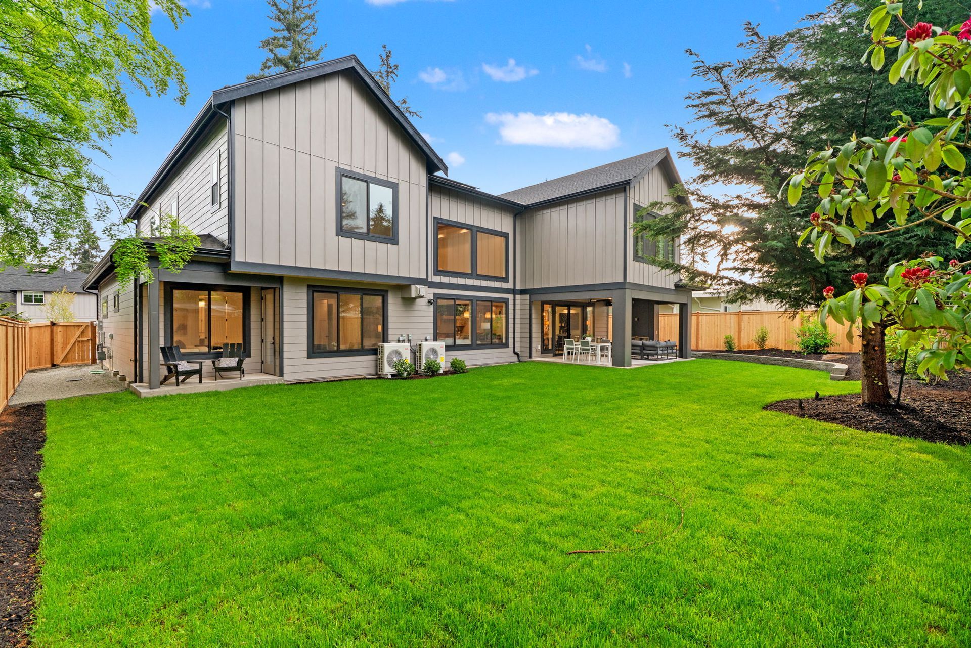 Modern two-story house with a large green lawn and trees in the yard