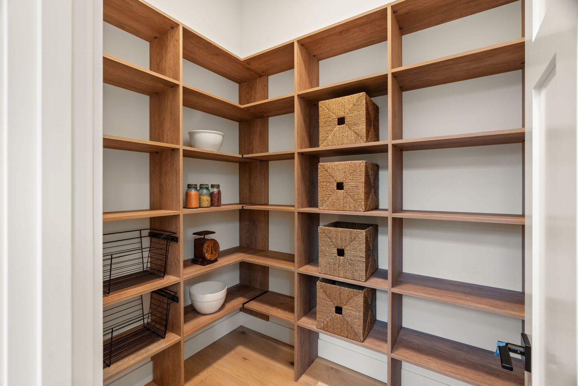 Wooden pantry with built-in shelves. Some shelves have baskets and bowls. Doorway on left.