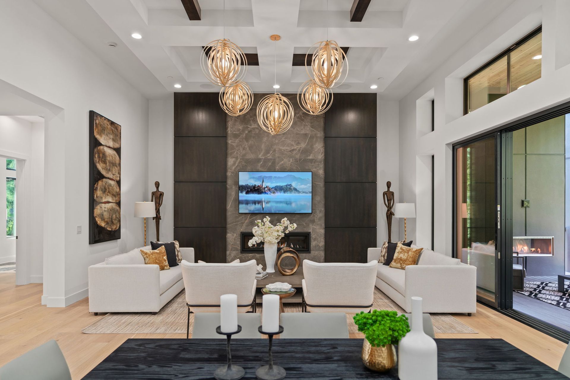 Luxurious living room with white sofas, gold chandeliers, fireplace, and dark accent wall.