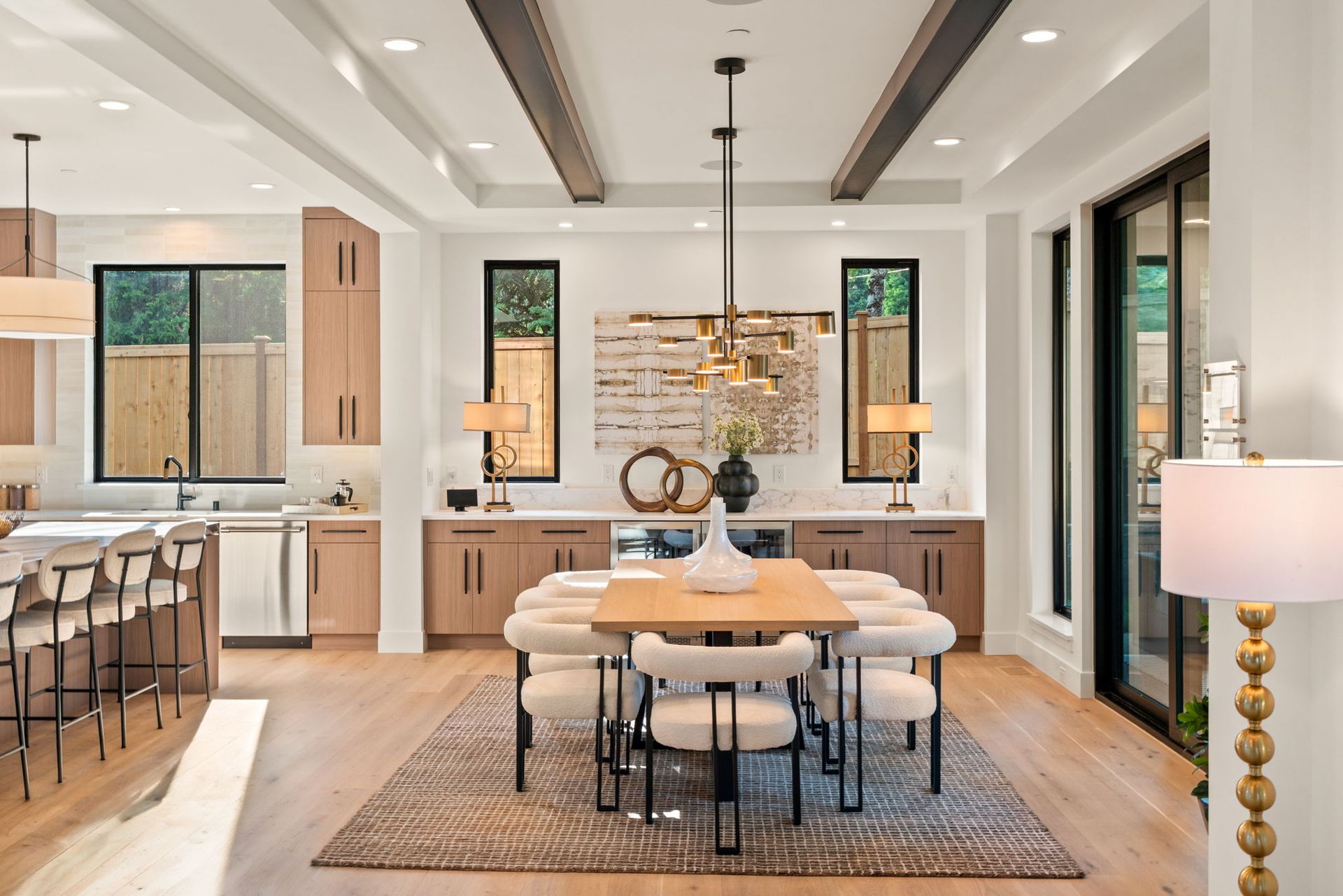 Modern open-plan dining room and kitchen with light wood accents, black chairs, and pendant lighting.