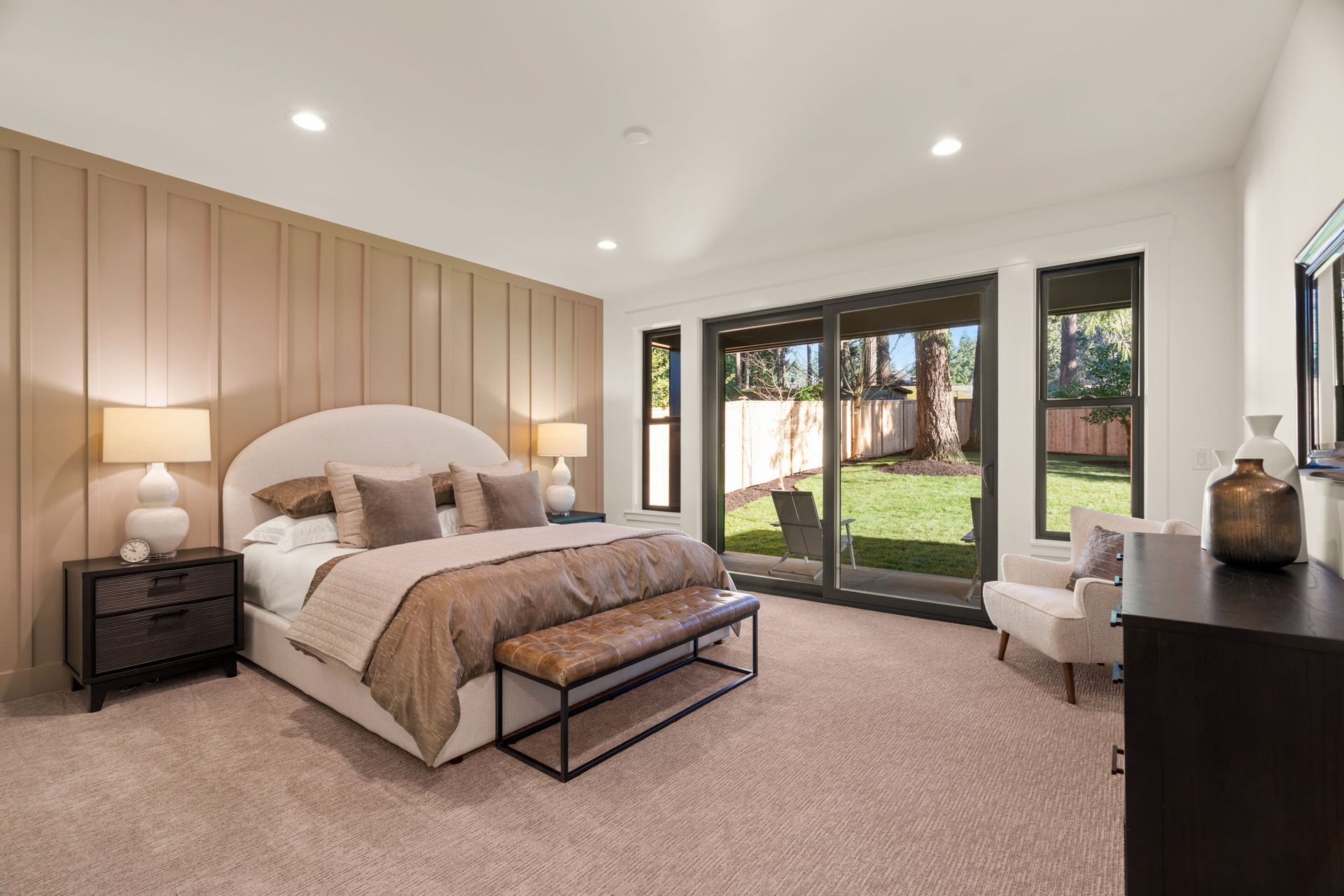 Bedroom with bed, bench, sliding doors to a green yard, light brown carpet, neutral colors.