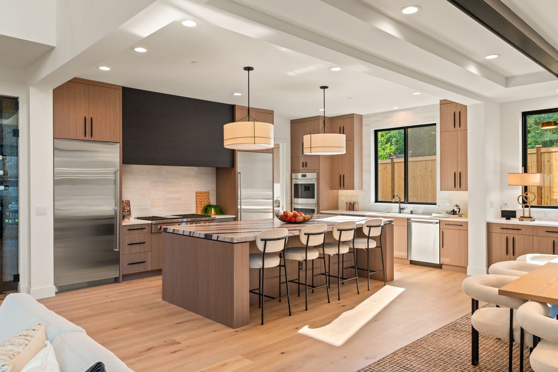 Modern kitchen with island, bar stools, wood cabinets, stainless fridge, and bright white ceiling beams
