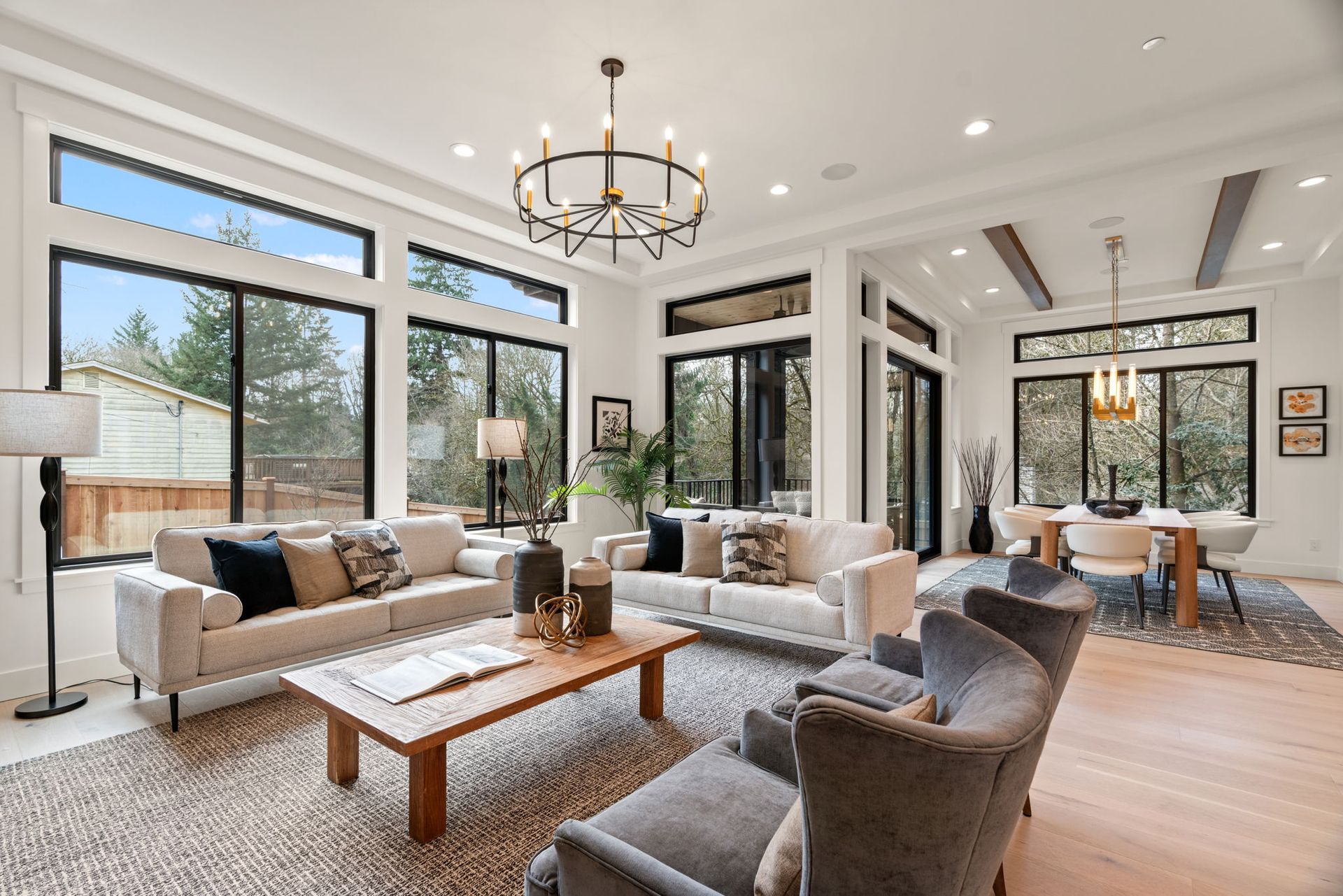Bright, modern living room with large windows, light sofas, and a dining area.