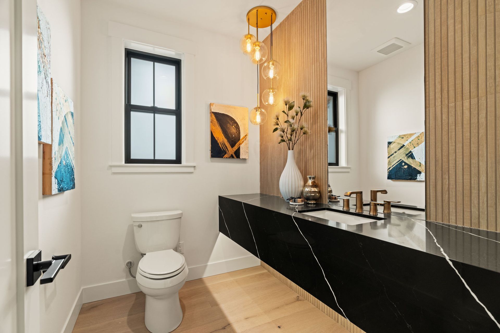Modern powder room with black countertop, gold light fixture, and artwork.