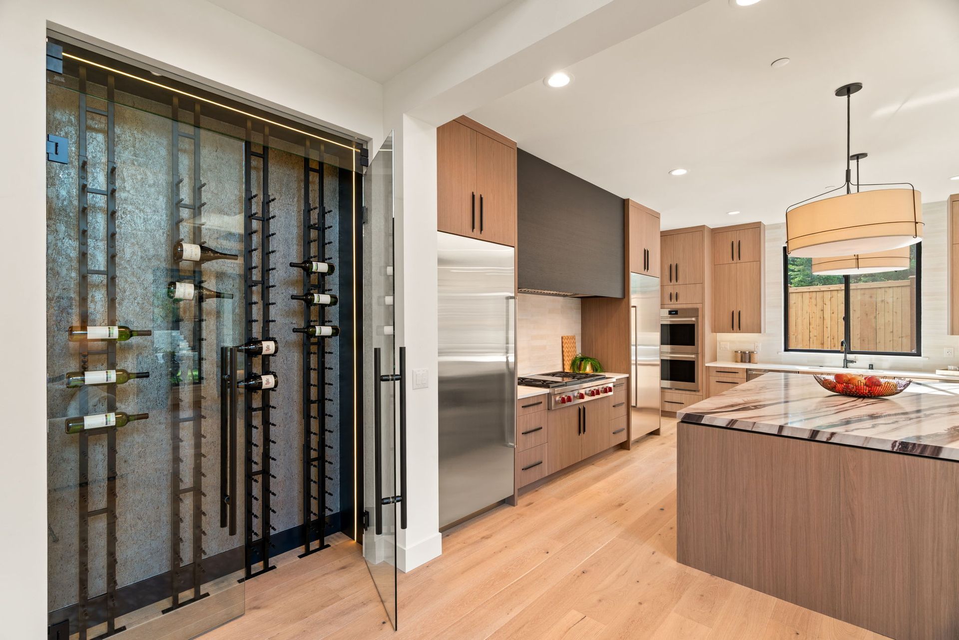 Modern kitchen with island, stainless fridge, wood cabinets, and a glass wine display door