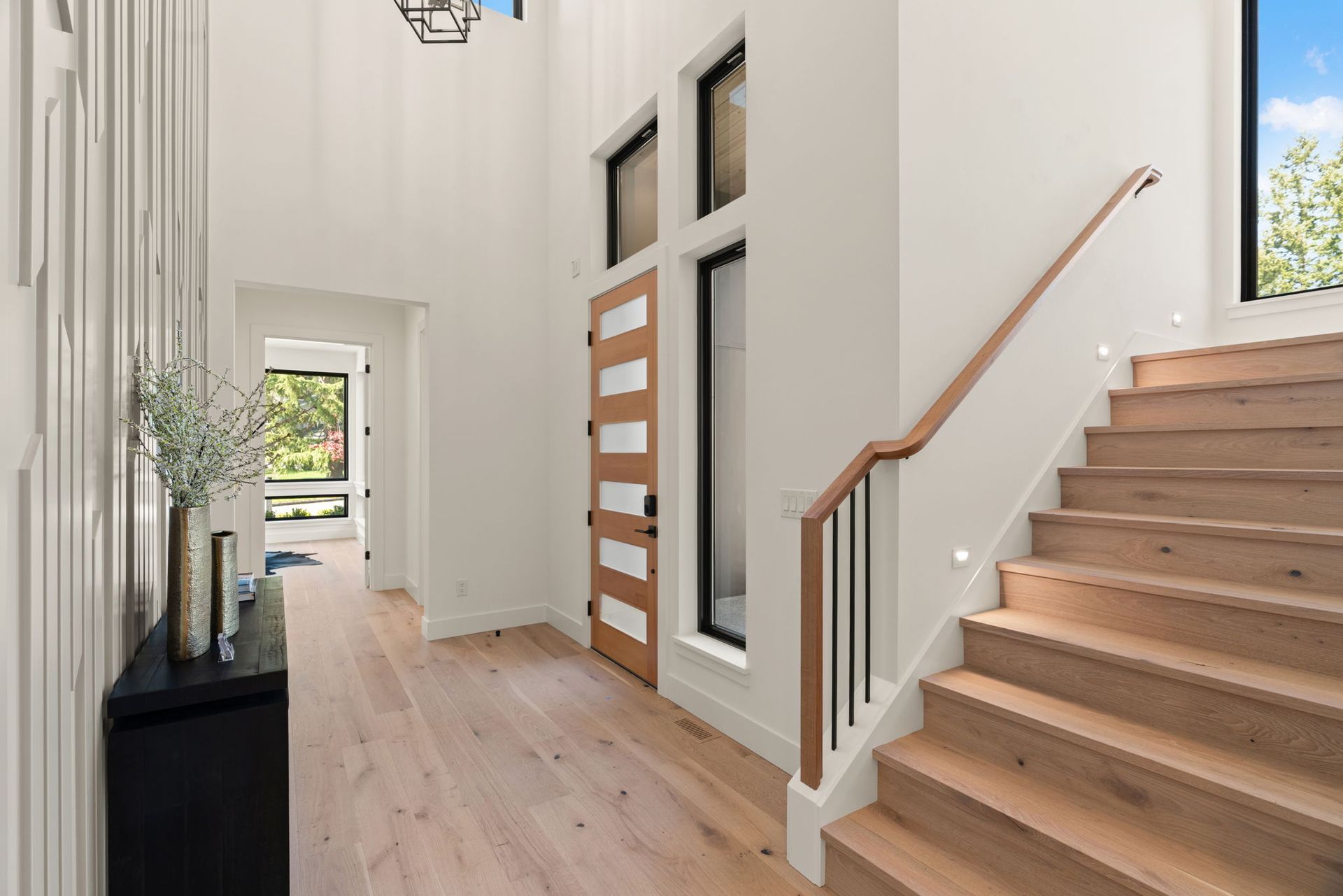 Bright modern entryway with wood stairs, white walls, and a hallway to a glass door.