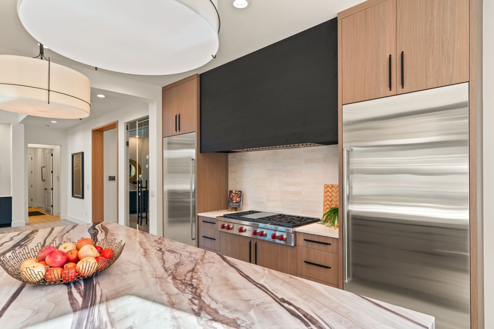 Modern kitchen with stainless steel appliances, wood cabinets, and a marble island with fruit bowl