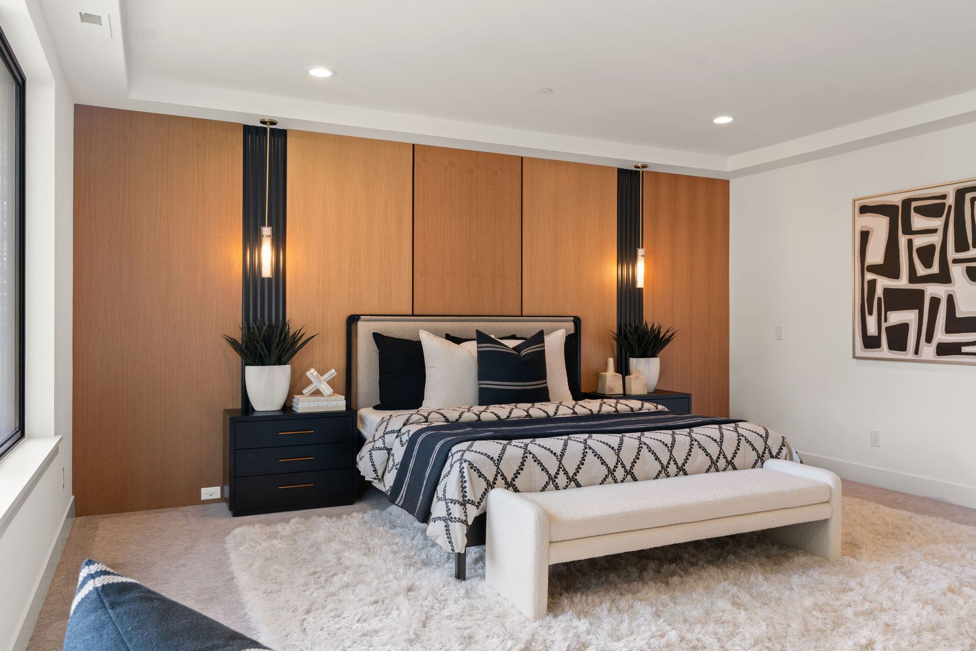 Modern bedroom with a bed, black nightstands, warm wood accent wall, and abstract wall art