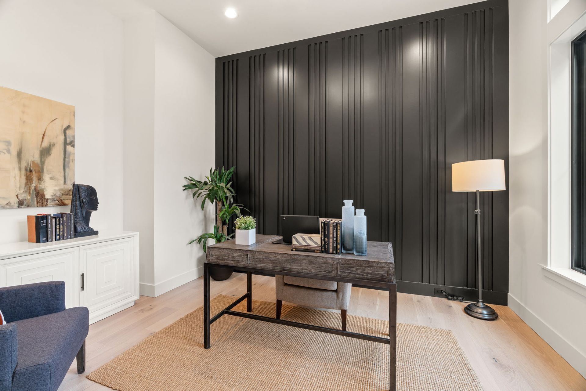 Home office with a black paneled wall, desk, rug, and a floor lamp.