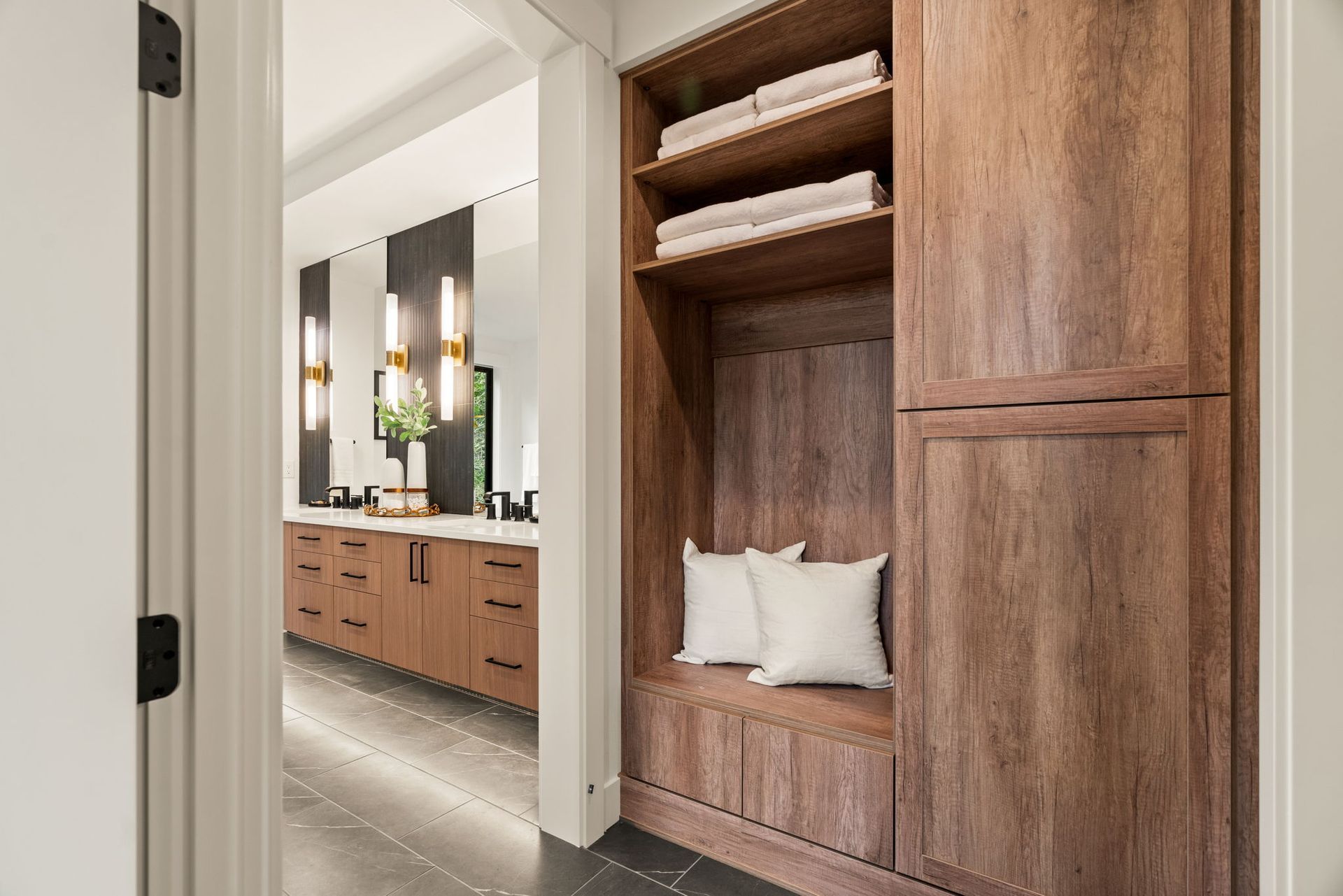 Bathroom hallway with built-in wooden storage, including shelves, a bench, and a cabinet. A large vanity is visible.
