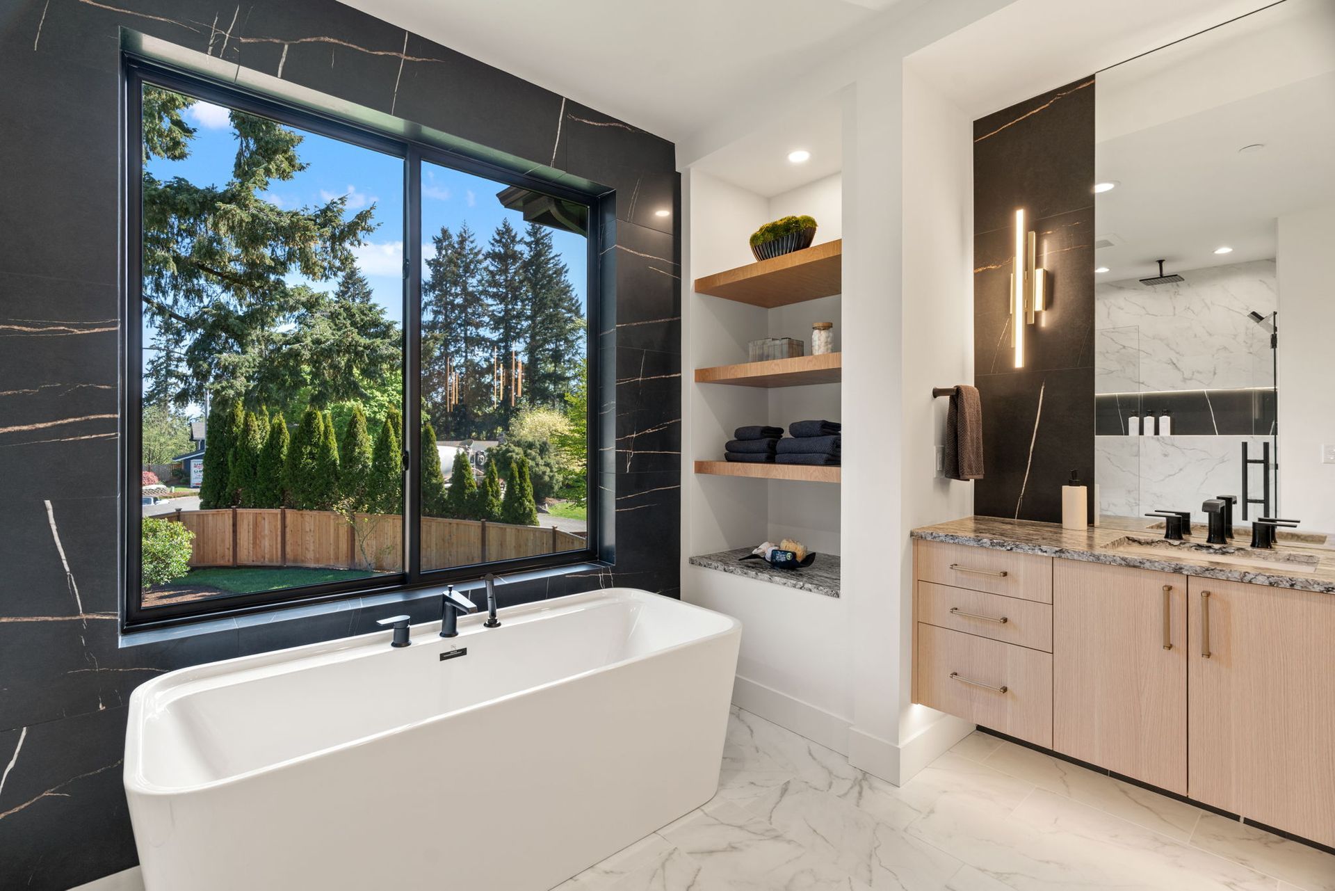 Modern bathroom with freestanding tub, black-framed window, and light wood vanity.