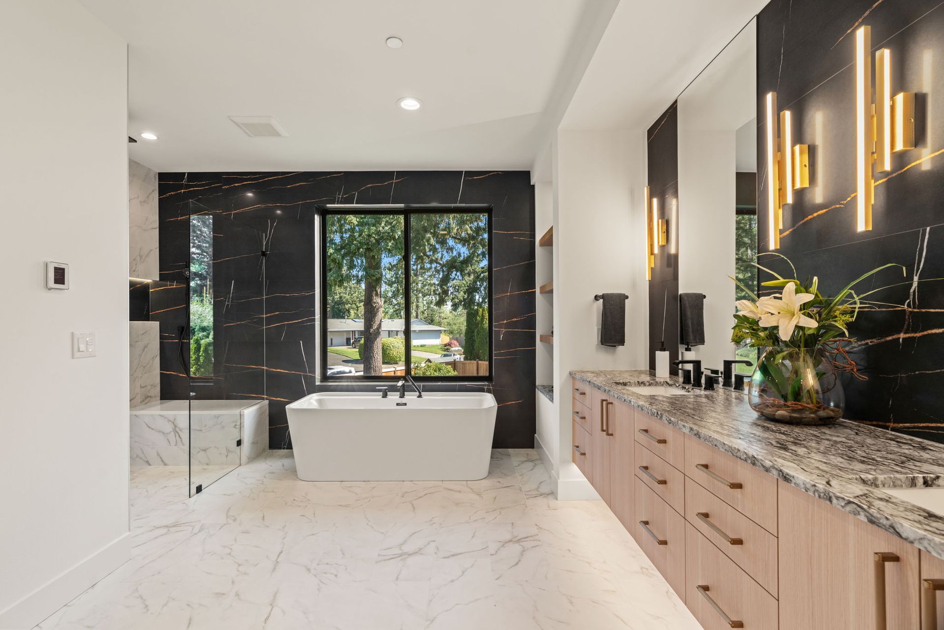 Modern white bathroom with freestanding tub, double vanity, and large window overlooking greenery