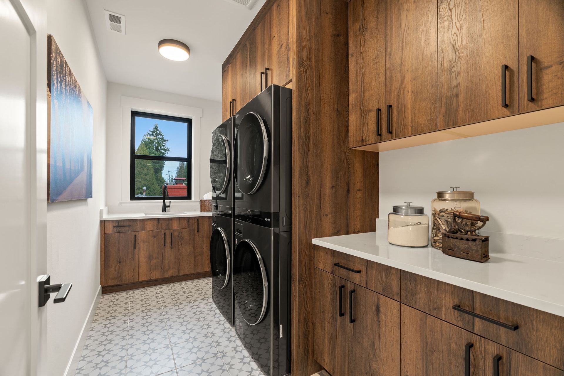 Laundry room with dark wood cabinets, black appliances, white countertops, and a patterned tile floor.