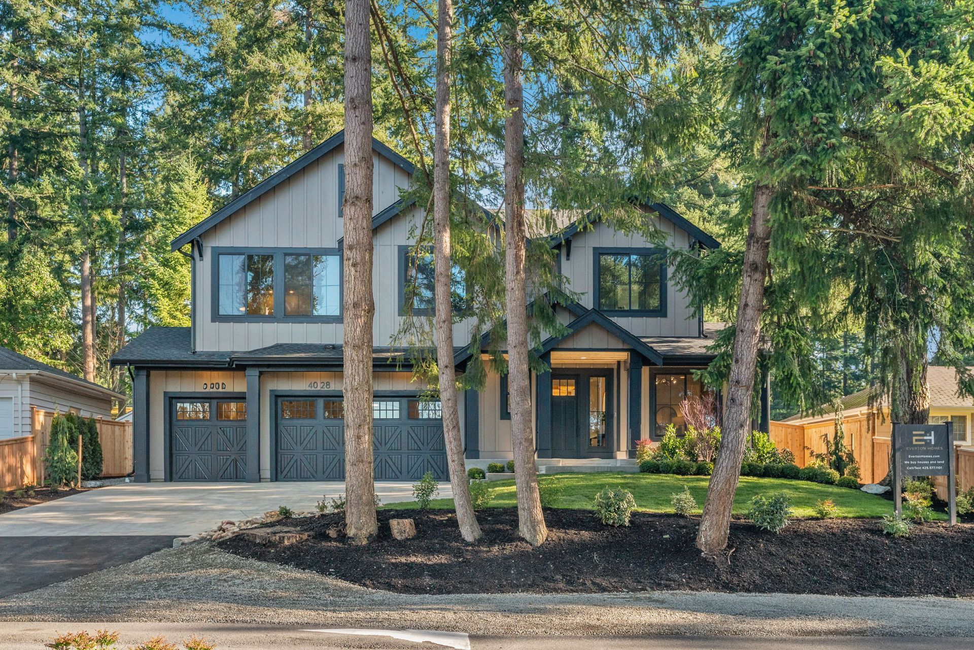 Modern two-story house with gray siding, black trim, and a two-car garage. Trees frame the facade.