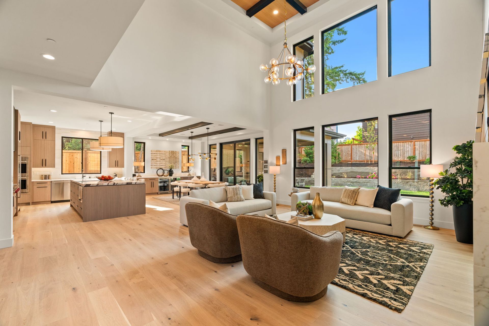 Bright open-plan living room with high ceilings, large windows, sectional sofa, and kitchen island