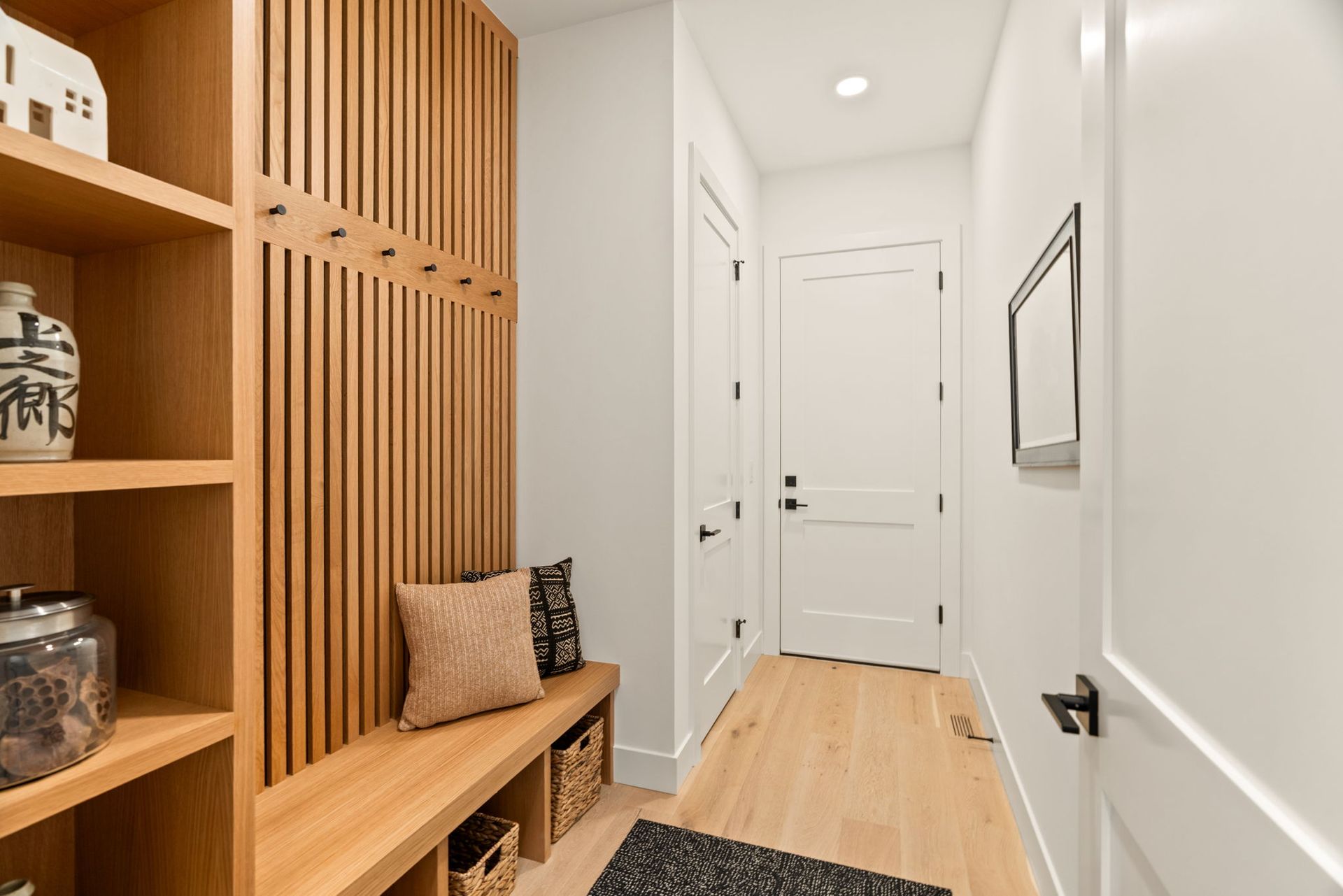 Bright mud room with wood bench and shelving, white doors, and a black runner rug