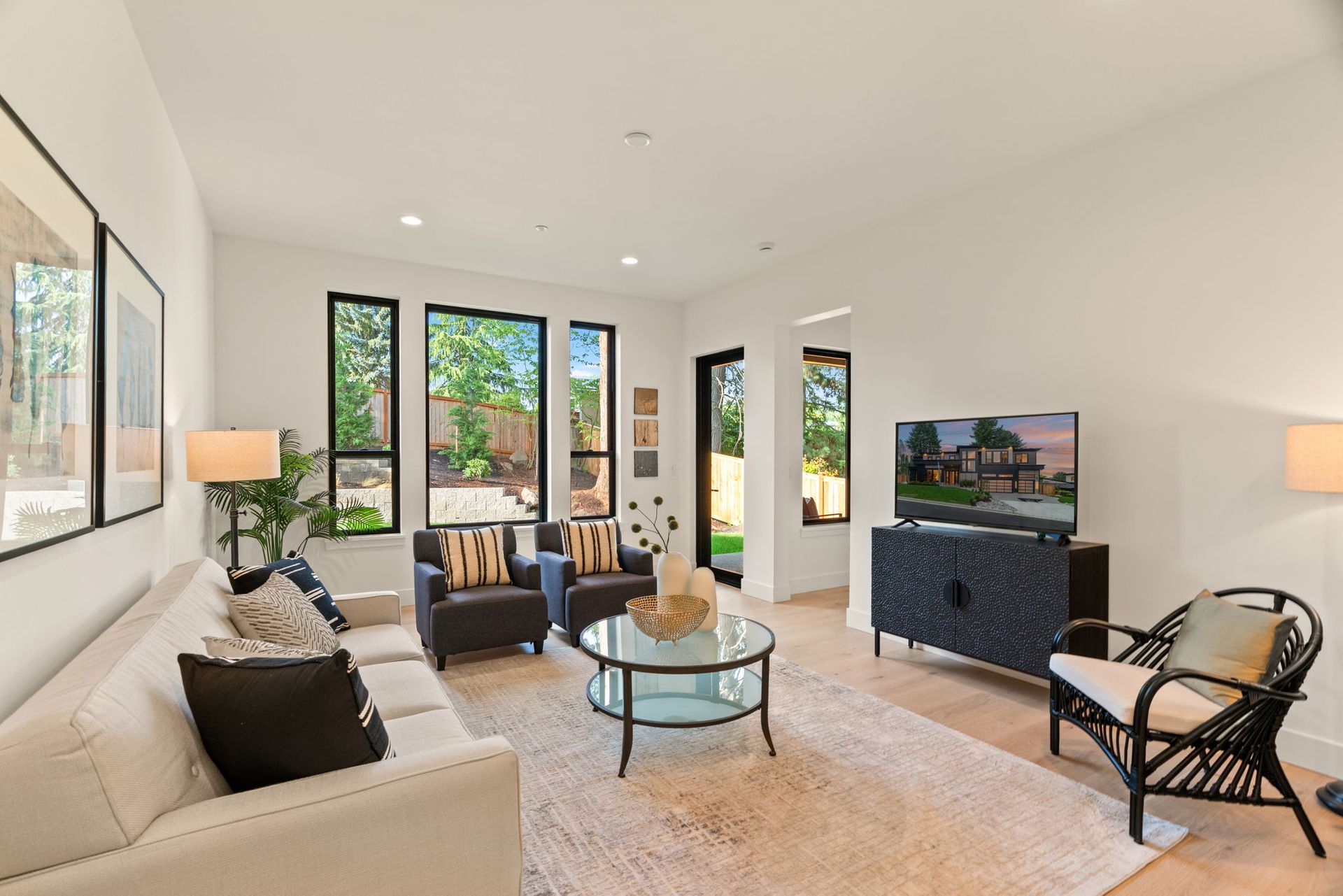 Bright modern bonus room with white sofa, glass coffee table, large windows, and TV on a dark console