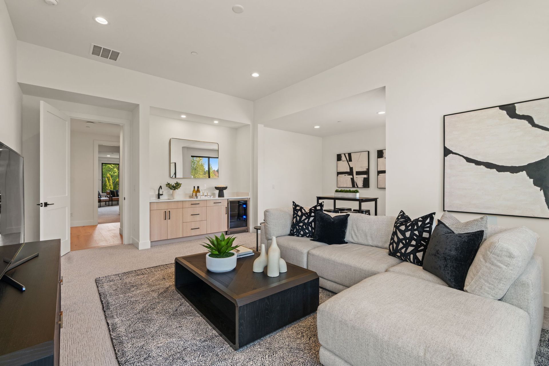 Bright modern living room with light gray sofa, black coffee table, and open kitchen view