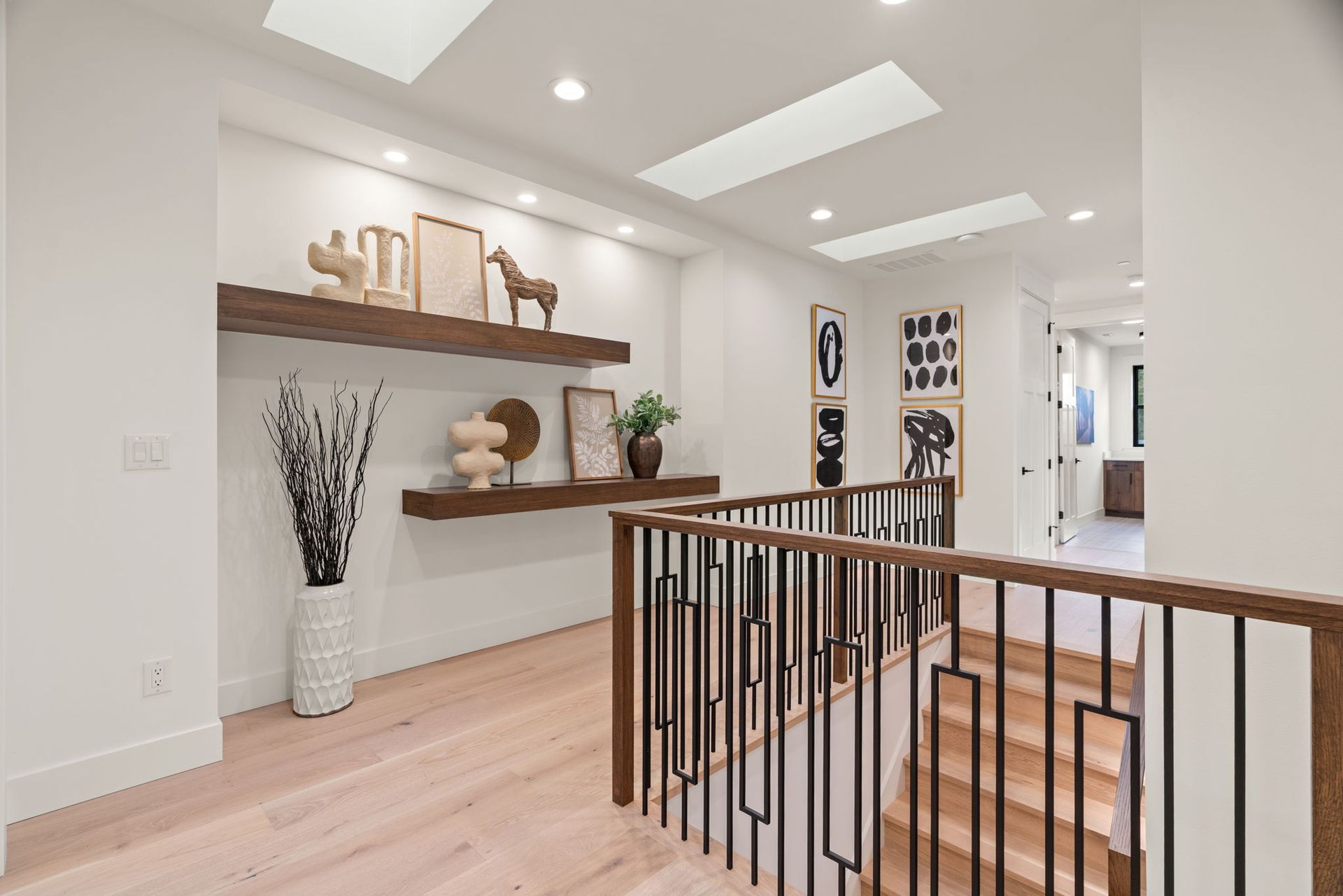 Hallway with wooden floors, floating shelves with decor, and a railing leading to stairs.