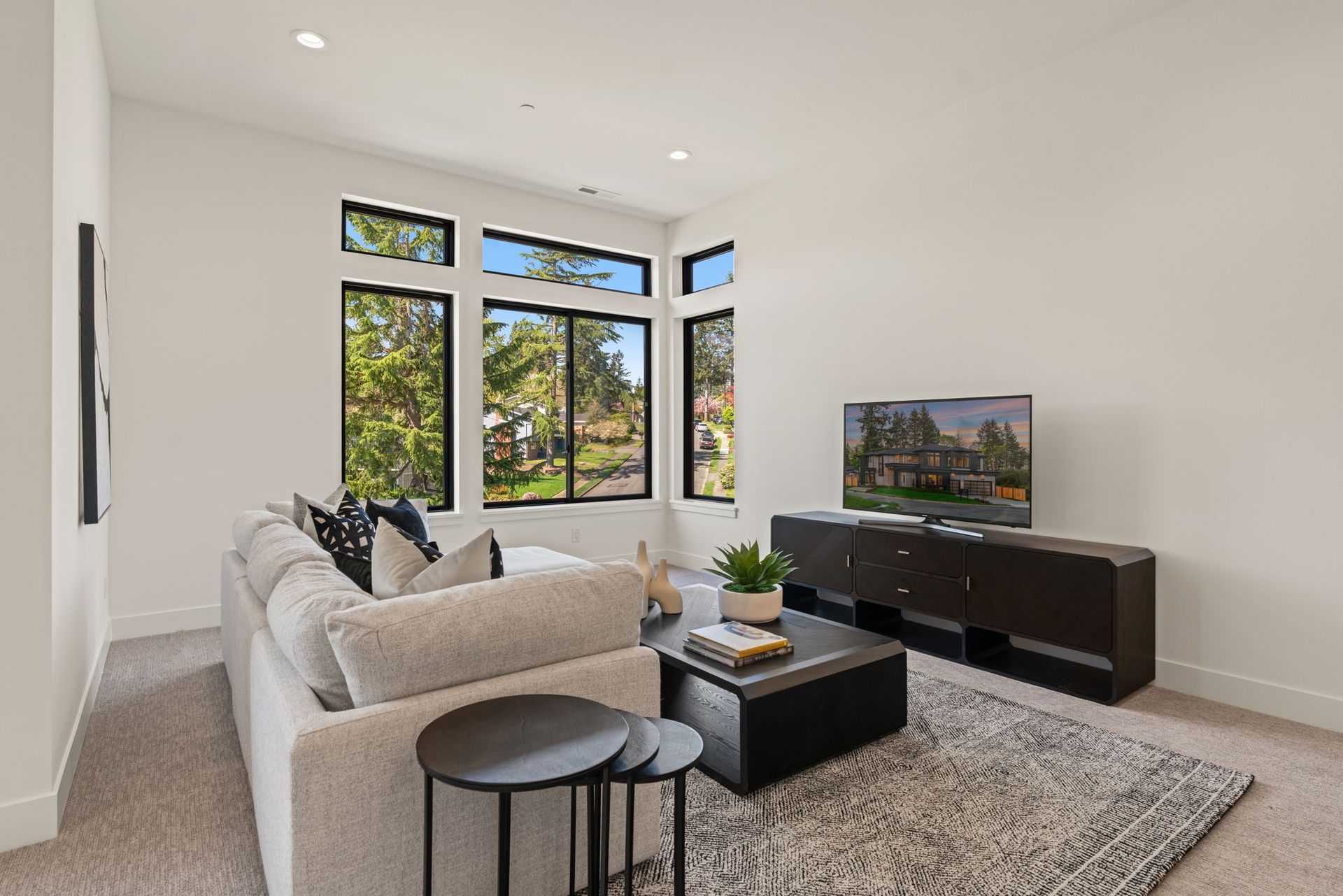 Modern living room with gray sofa, TV, large windows, and white walls