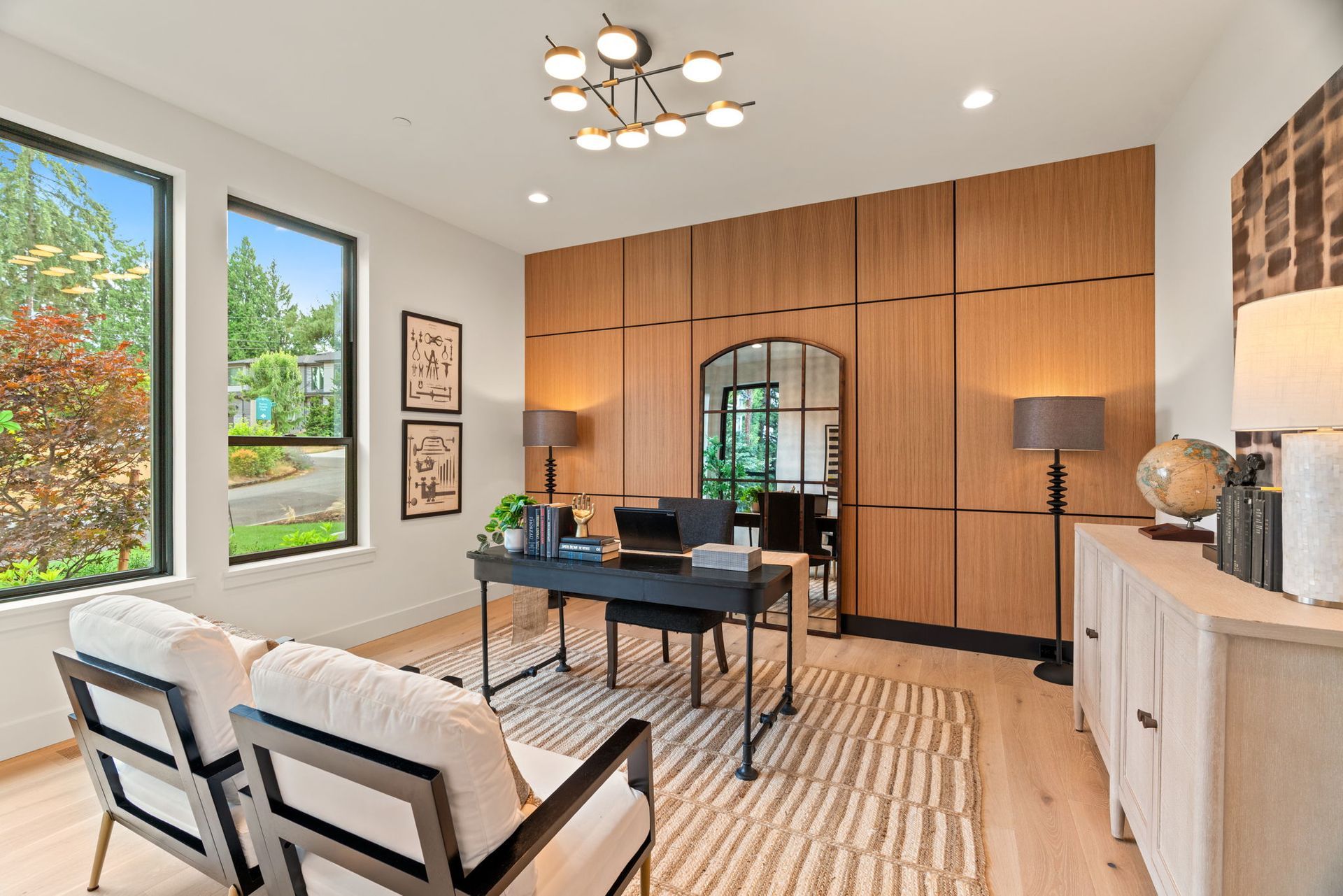 Bright modern home office with wood-paneled wall, desk, chairs, large windows, and striped rug