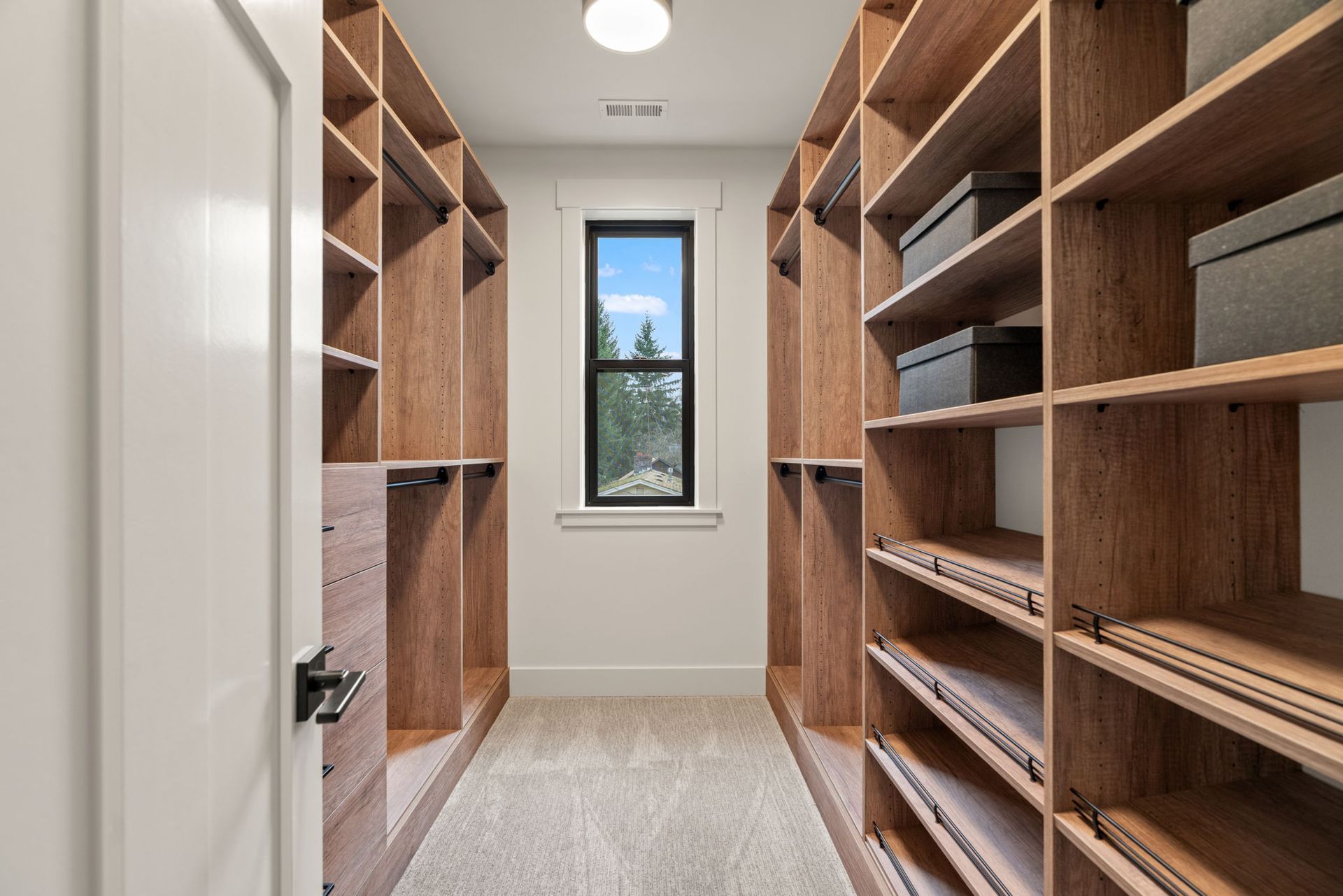 Walk-in closet with wood shelves, clothes rods, and a window. Light-colored carpet and neutral walls.