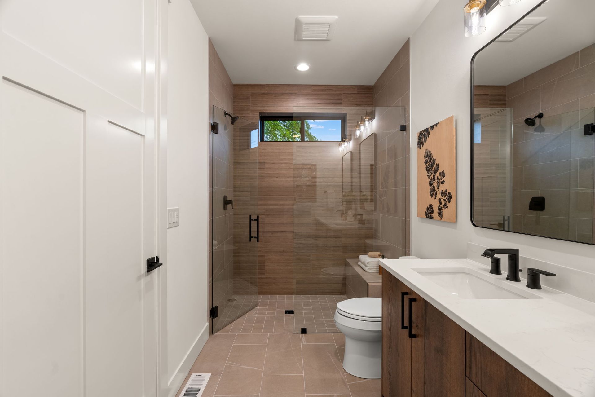 Modern bathroom with white vanity, toilet, walk-in shower, and beige tile walls