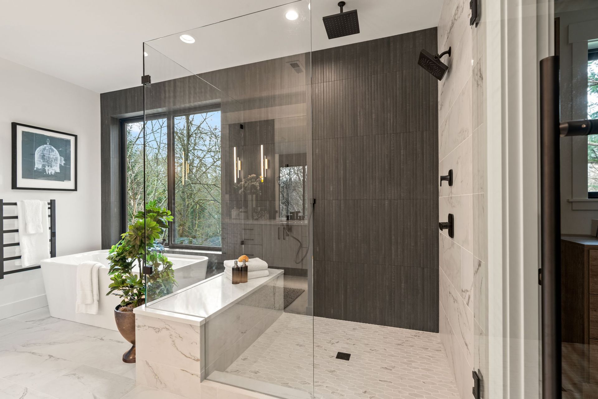 Modern bathroom with large glass shower, tub, and vanity; neutral tones, natural light, and outdoor view.