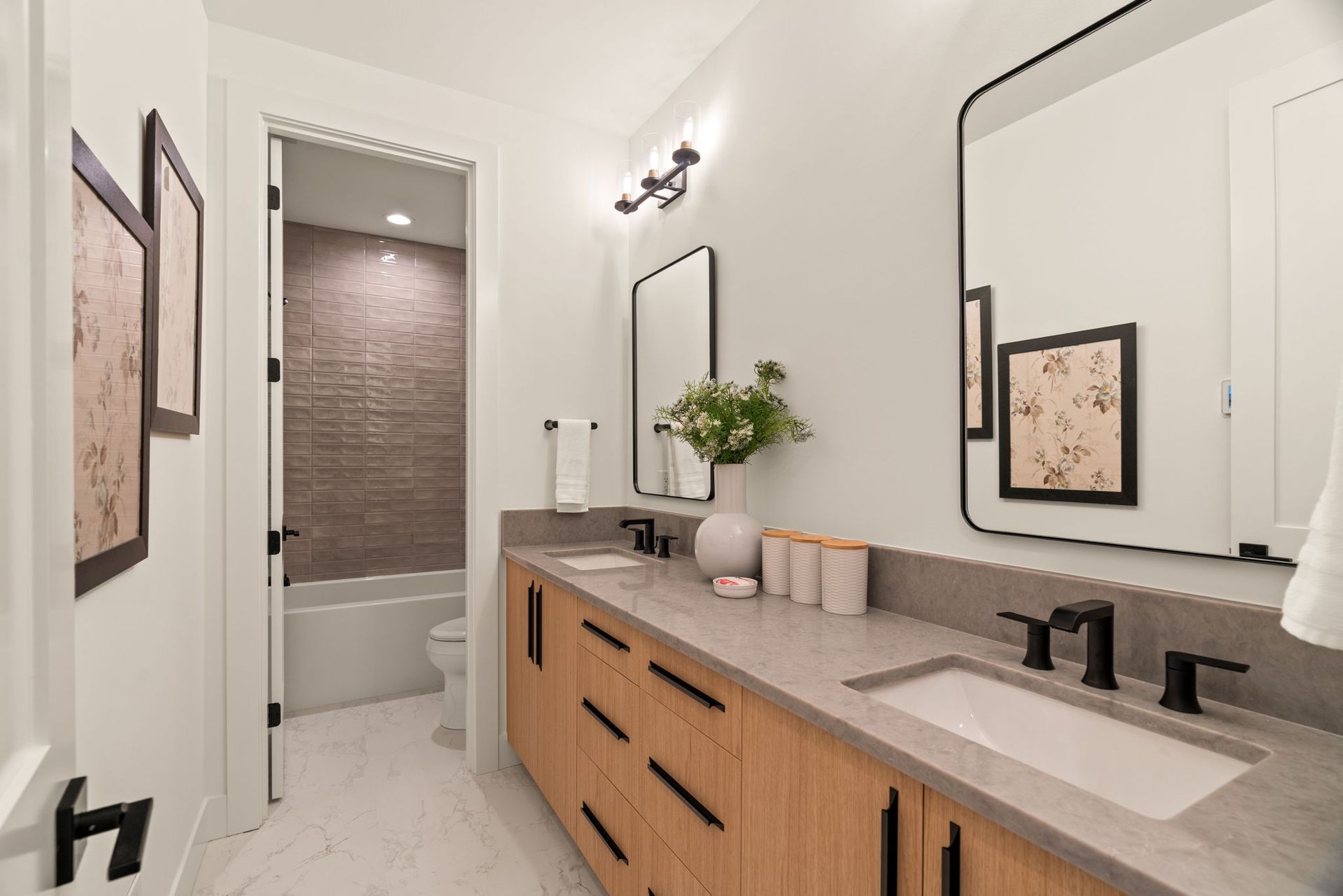 Modern bathroom with double vanity, large mirror, wall sconces, and a tub in the background