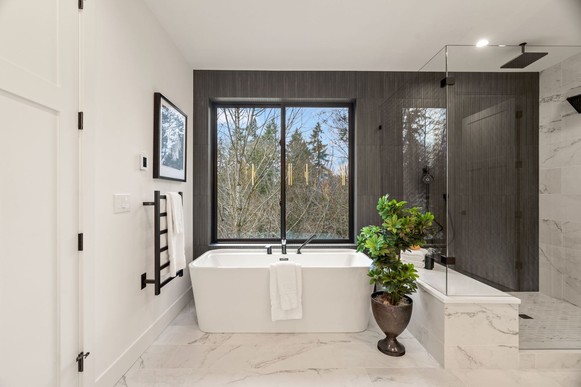 Modern bathroom with a white tub, large window overlooking trees, and dark accent wall.