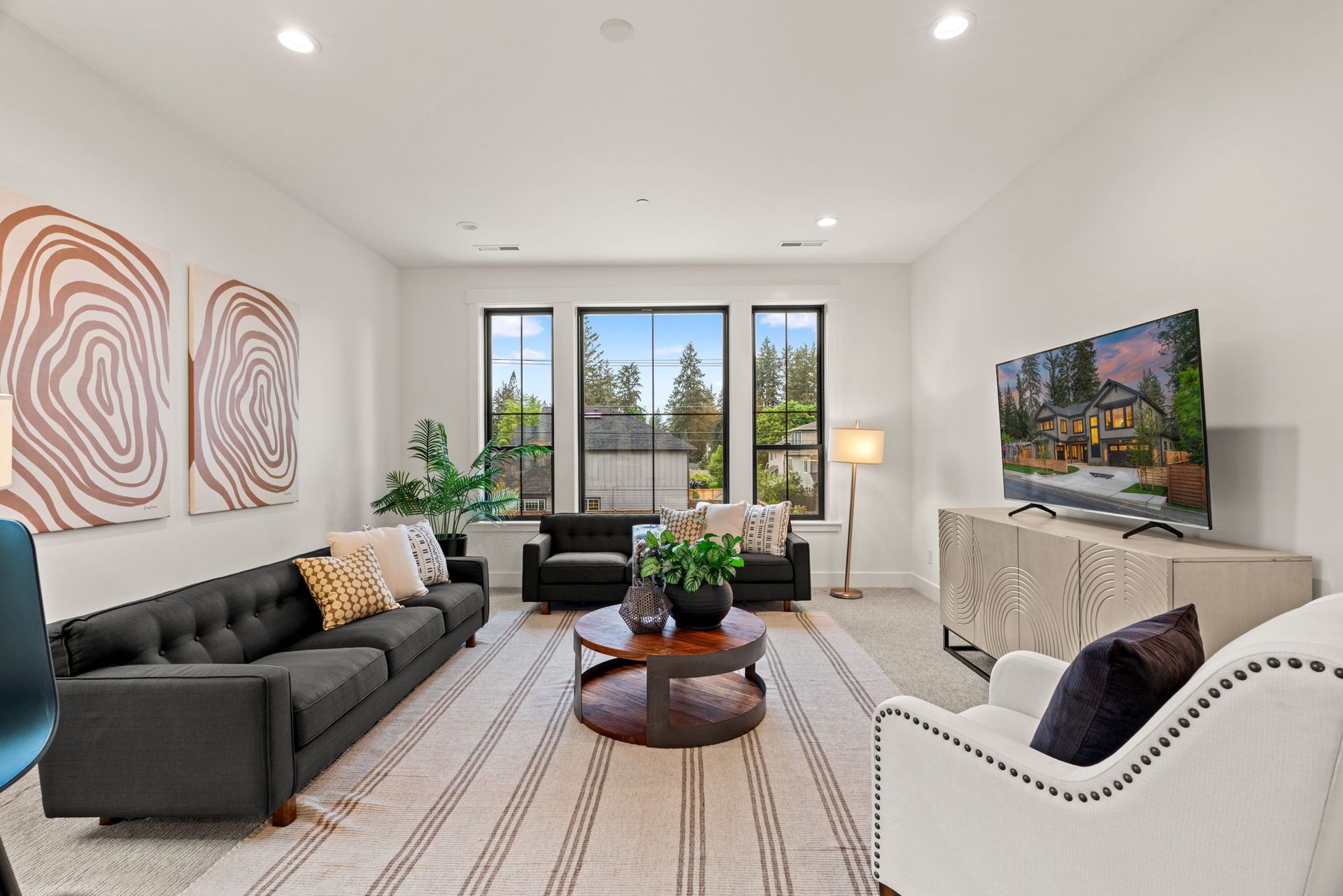 Modern living room with dark gray sofa, white chair, fireplace, striped rug, and large windows.